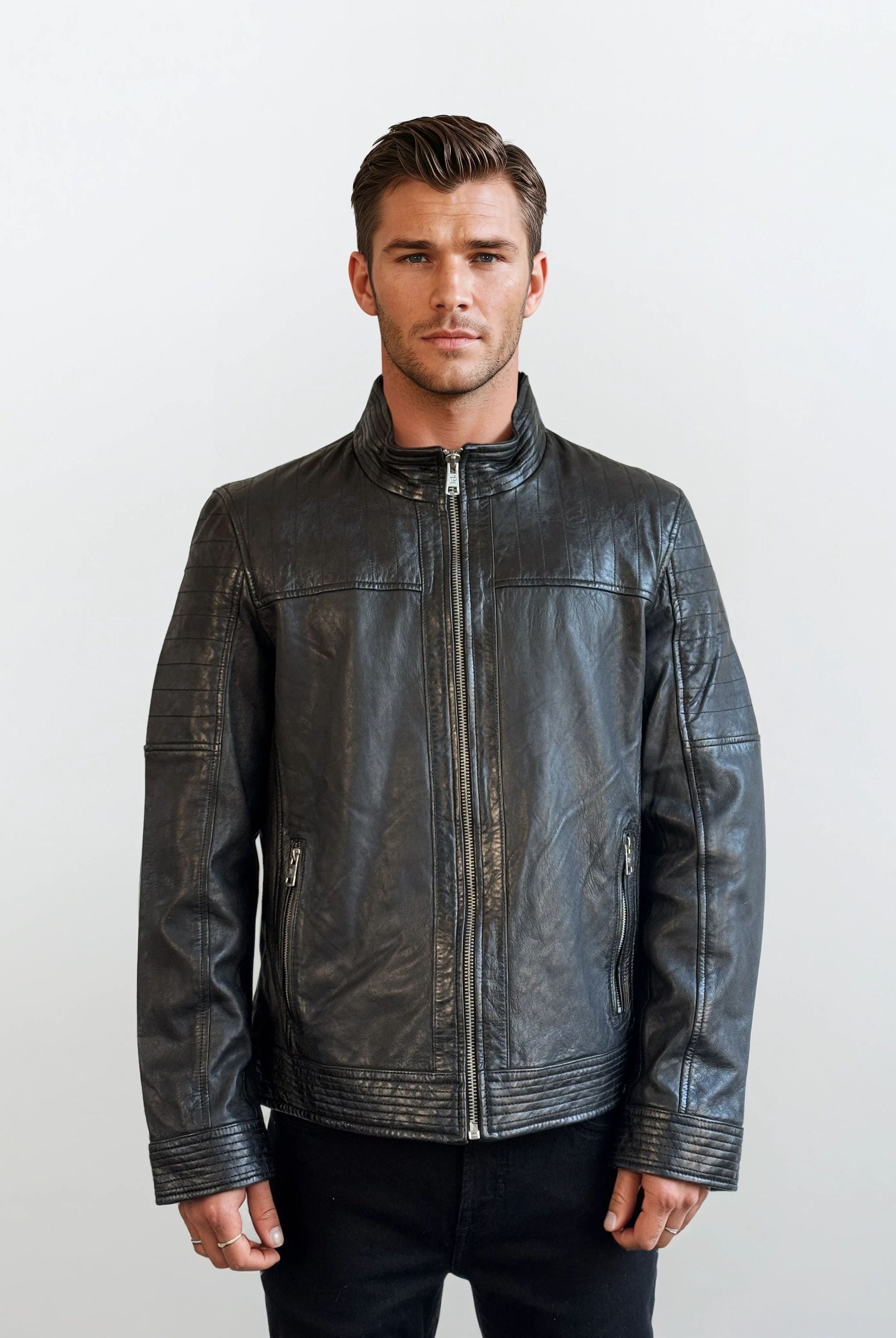 Ein Mann mit kurzen braunen Haaren steht vor einem schlichten Hintergrund, trägt eine trueprodigy Herren Lederjacke aus Schafsleder in Schwarz mit klassischem Blouson-Schnitt und eine schwarze Hose und zeigt einen neutralen Ausdruck.