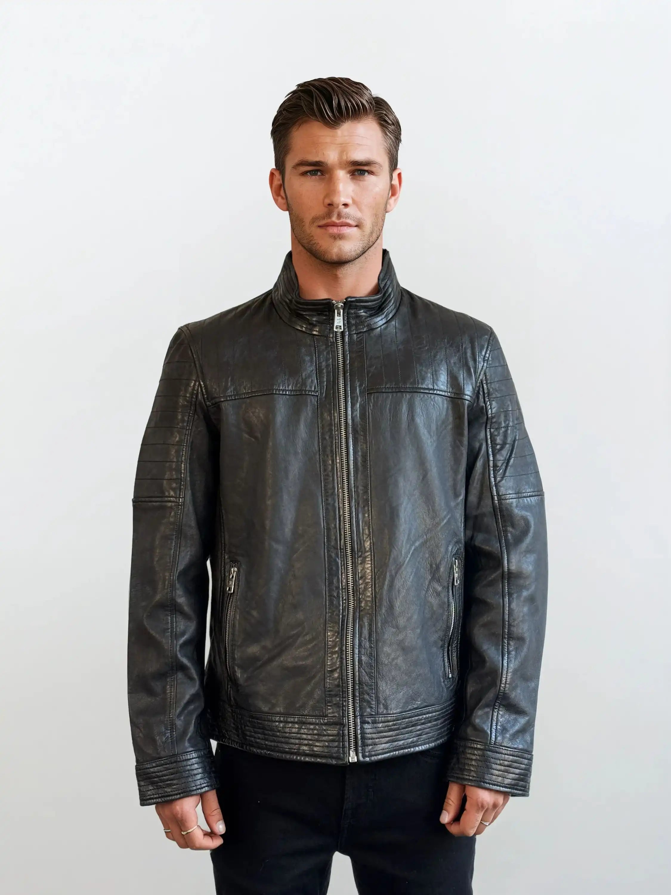 Ein Mann mit kurzen braunen Haaren steht vor einem schlichten Hintergrund, trägt eine trueprodigy Herren Lederjacke aus Schafsleder in Schwarz mit klassischem Blouson-Schnitt und eine schwarze Hose und zeigt einen neutralen Ausdruck.