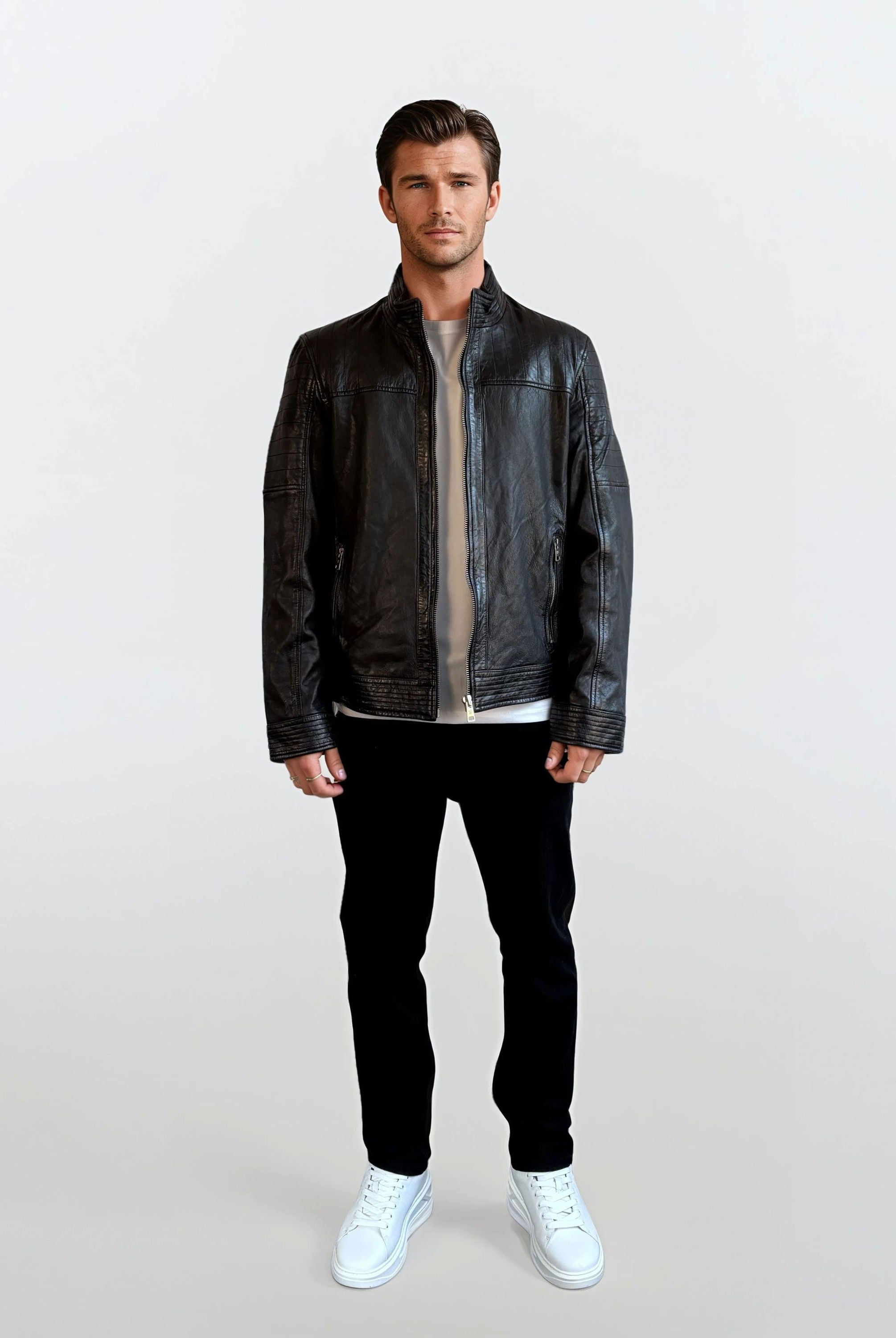 Ein Mann trägt die trueprodigy Herren Lederjacke aus Schafsleder in Schwarz mit klassischem Blouson-Schnitt über einem beigen Shirt, kombiniert mit schwarzen Hosen und weißen Sneakern vor hellem Hintergrund.