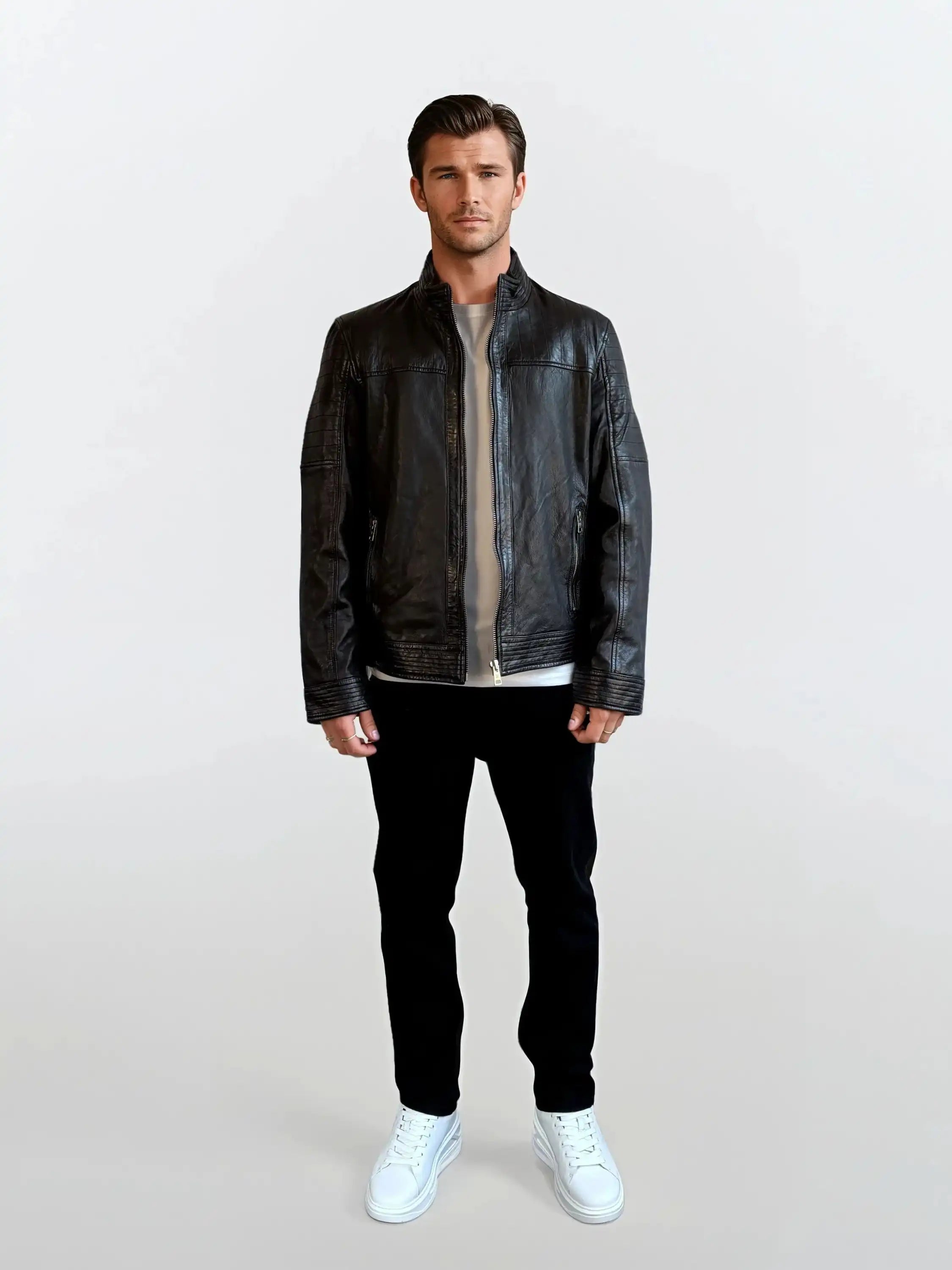 Ein Mann trägt die trueprodigy Herren Lederjacke aus Schafsleder in Schwarz mit klassischem Blouson-Schnitt über einem beigen Shirt, kombiniert mit schwarzen Hosen und weißen Sneakern vor hellem Hintergrund.