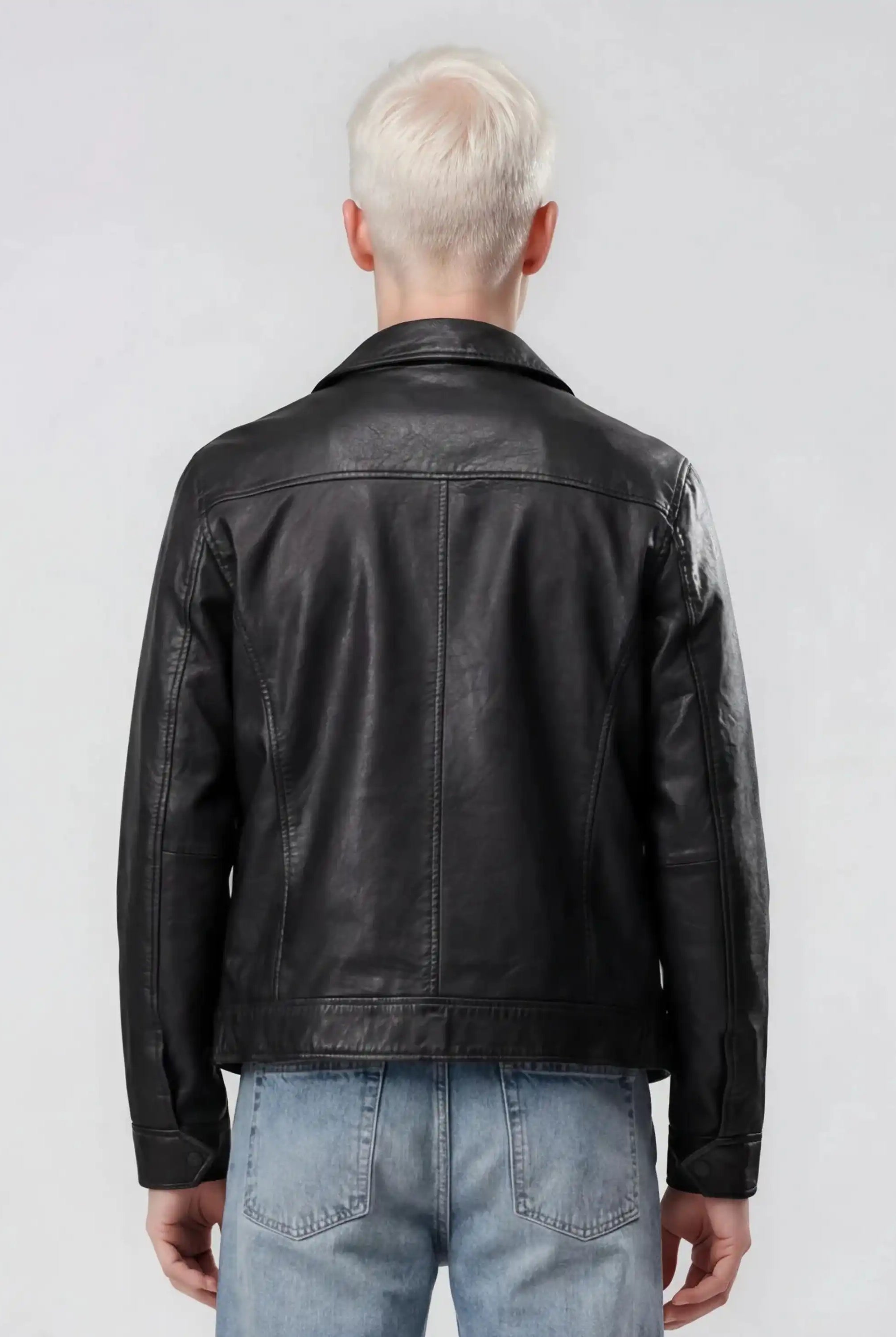 Gezeigt wird eine Person mit kurzen, hellblonden Haaren von hinten, die die trueprodigy Herren Lederjacke aus Schafsleder in Schwarz mit Hemd-Design und hellblaue Jeans vor einem schlichten hellgrauen Hintergrund trägt.
