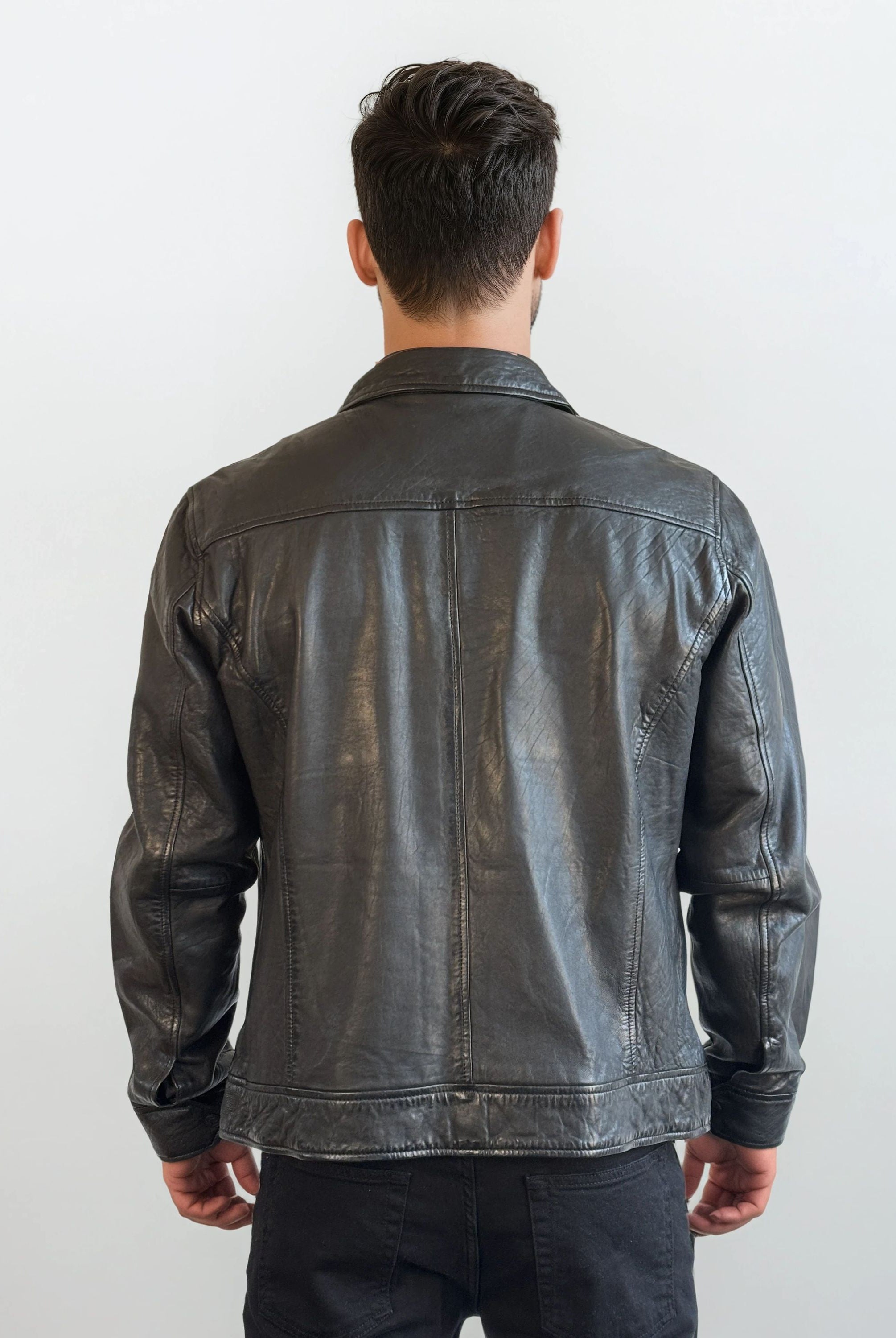 Eine Person mit kurzem, dunklem Haar trägt die trueprodigy Herren Lederjacke aus Schafsleder in Schwarz mit Hemd-Design sowie schwarzen Hosen und steht vor einem schlichten weißen Hintergrund.