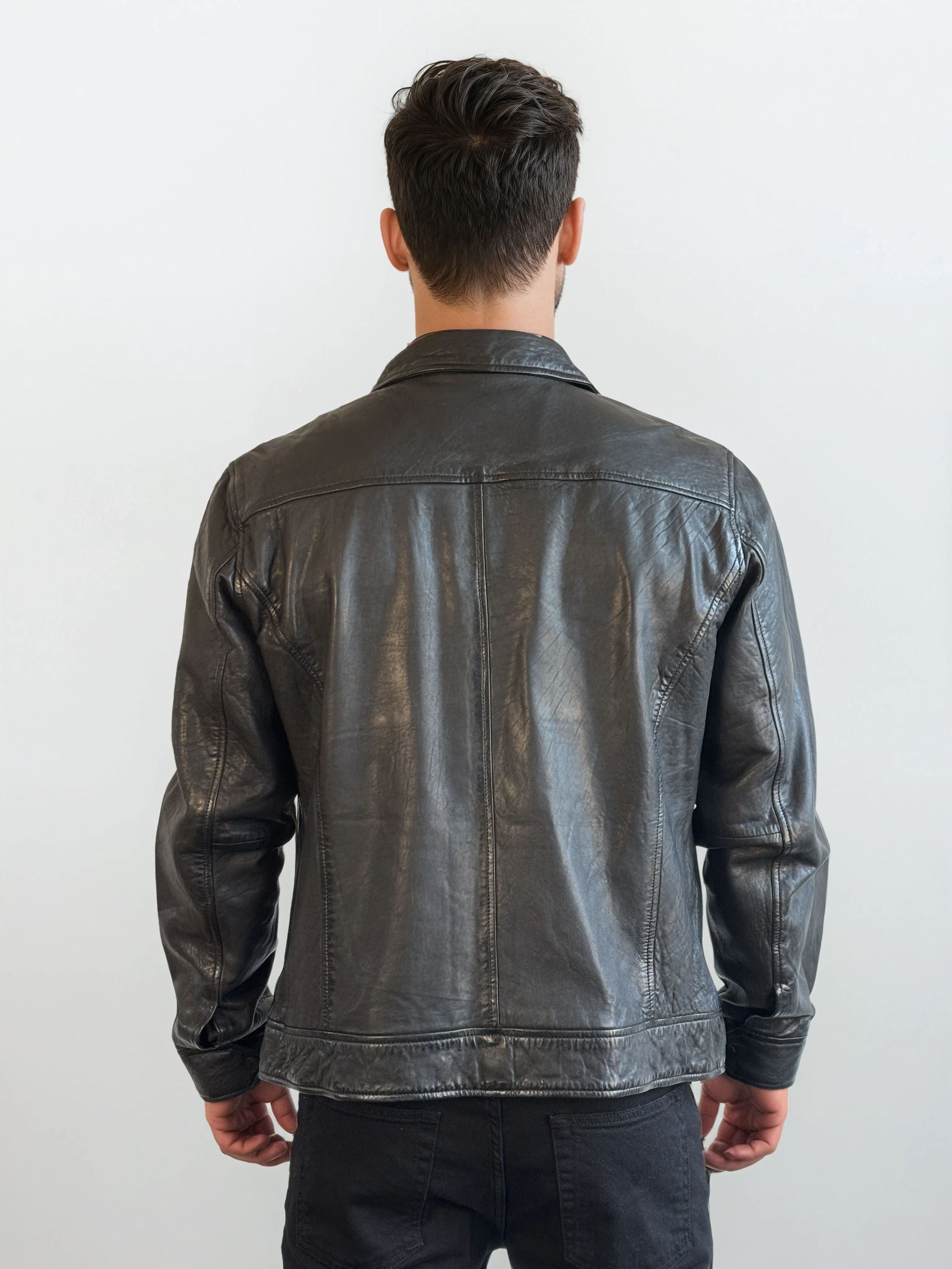 Eine Person mit kurzem, dunklem Haar trägt die trueprodigy Herren Lederjacke aus Schafsleder in Schwarz mit Hemd-Design sowie schwarzen Hosen und steht vor einem schlichten weißen Hintergrund.