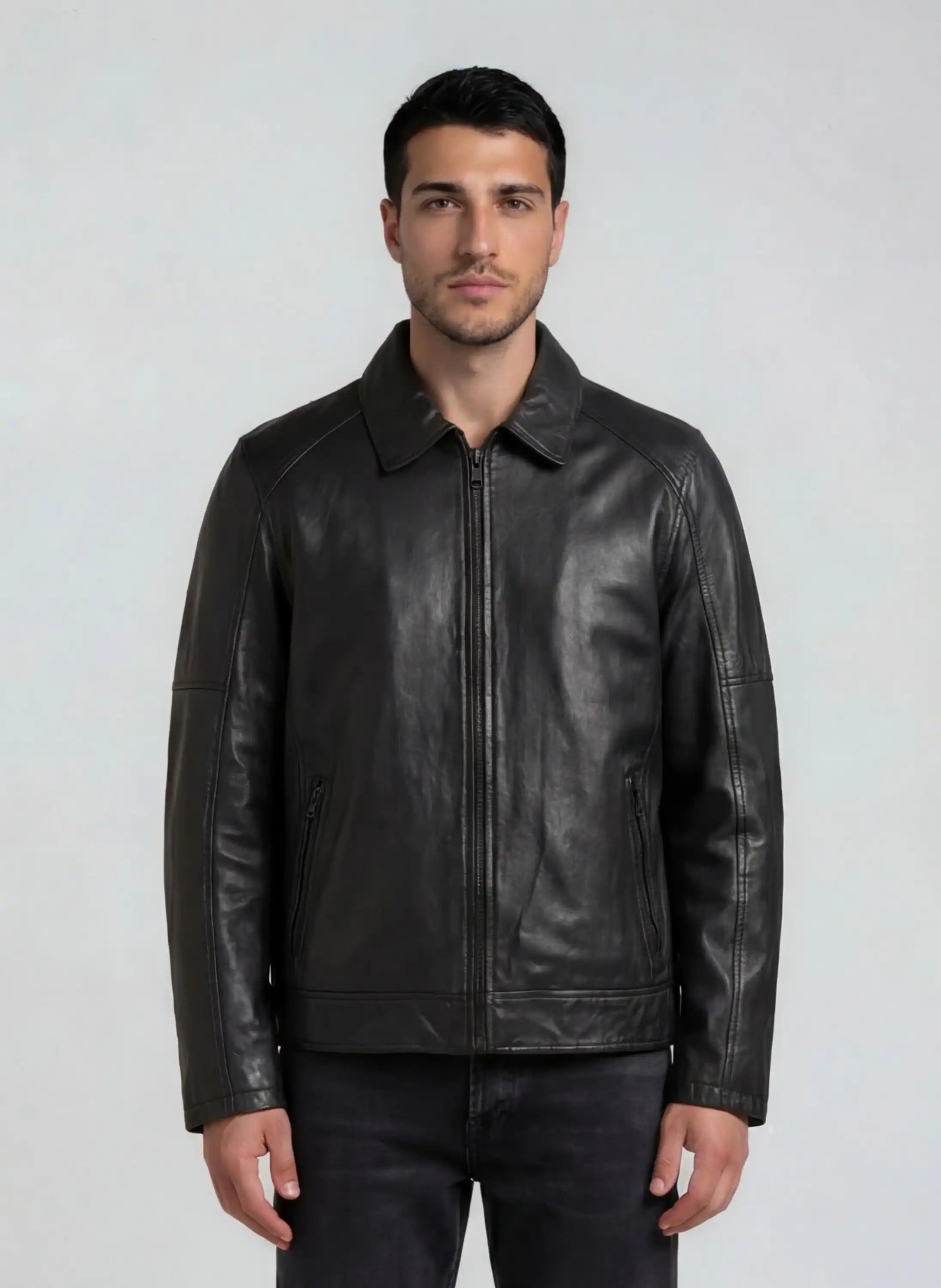 Ein Mann mit kurzen dunklen Haaren trägt die trueprodigy Herren Lederjacke aus Schafsleder in Schwarz mit Ärmel-Reißverschlüssen über einem dunklen Hemd und Jeans und steht mit neutralem Gesichtsausdruck vor einem schlichten hellen Hintergrund.
