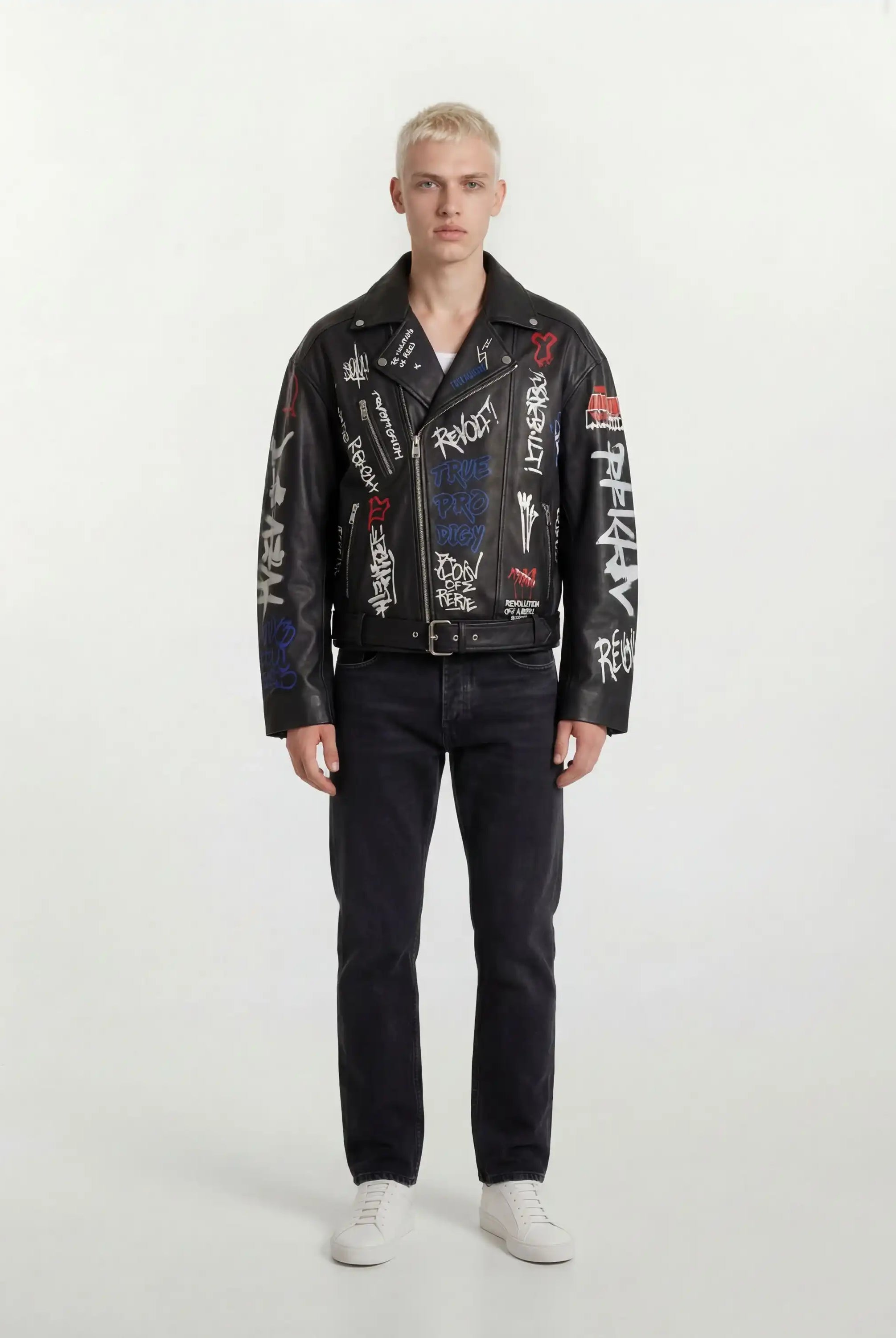 Eine Person mit kurzen blonden Haaren schaut nach vorne und trägt eine trueprodigy Herren Lederjacke aus Schafsleder in Schwarz mit Graffiti-Prints, gepaart mit schwarzen Jeans und weißen Turnschuhen vor einem schlichten hellen Hintergrund.