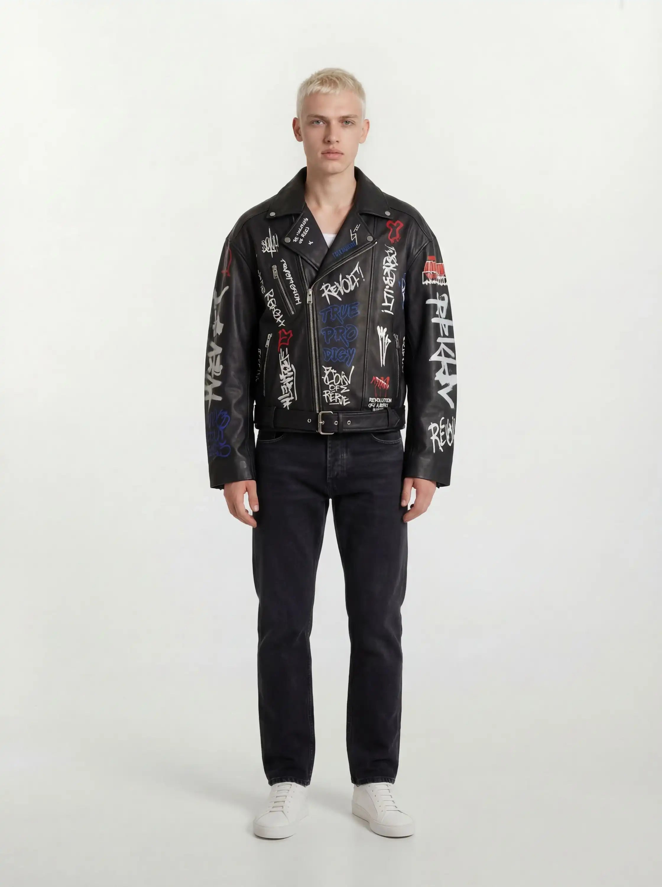 Eine Person mit kurzen blonden Haaren schaut nach vorne und trägt eine trueprodigy Herren Lederjacke aus Schafsleder in Schwarz mit Graffiti-Prints, gepaart mit schwarzen Jeans und weißen Turnschuhen vor einem schlichten hellen Hintergrund.