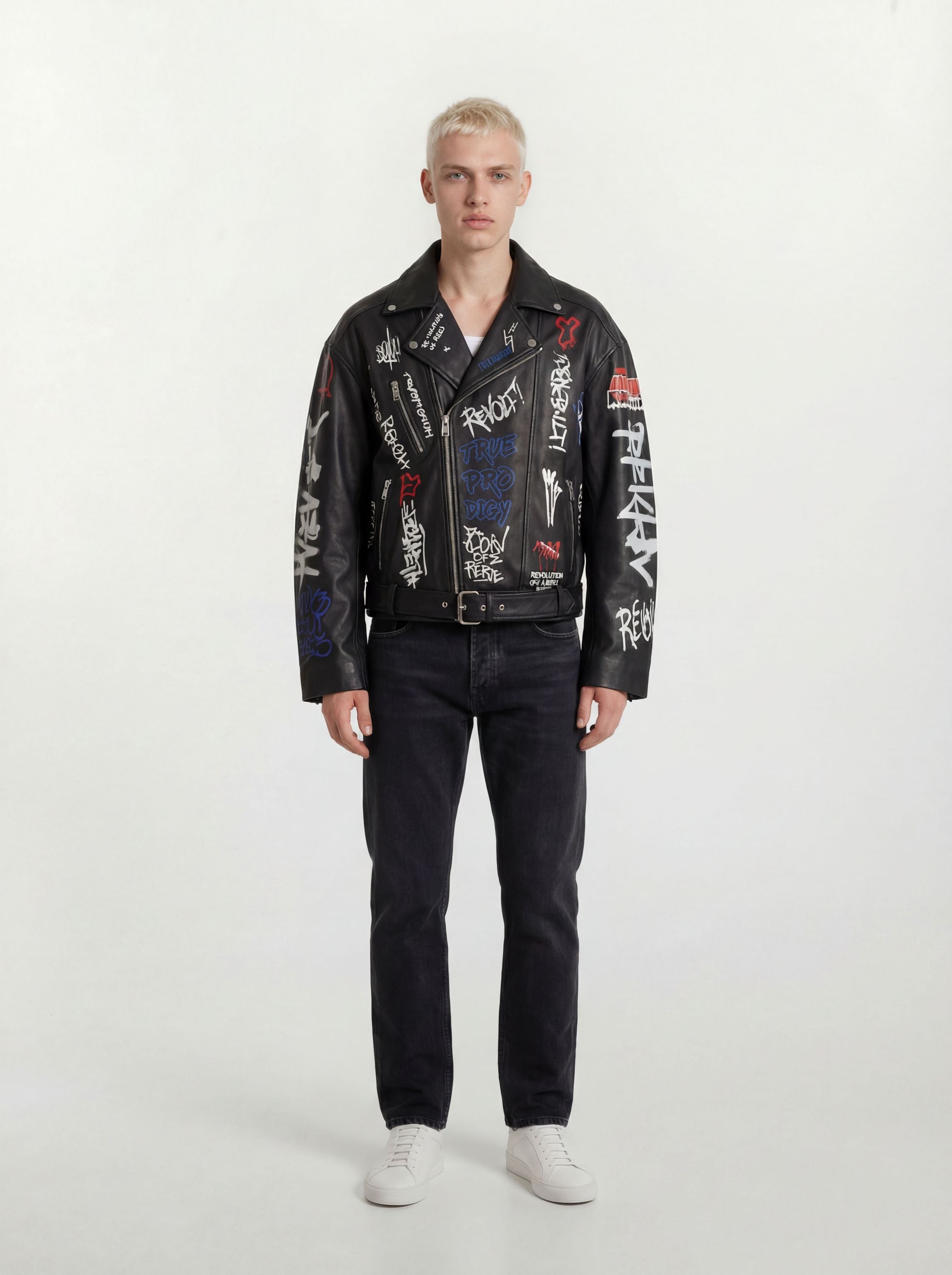 Eine Person mit kurzen blonden Haaren schaut nach vorne und trägt eine trueprodigy Herren Lederjacke aus Schafsleder in Schwarz mit Graffiti-Prints, gepaart mit schwarzen Jeans und weißen Turnschuhen vor einem schlichten hellen Hintergrund.