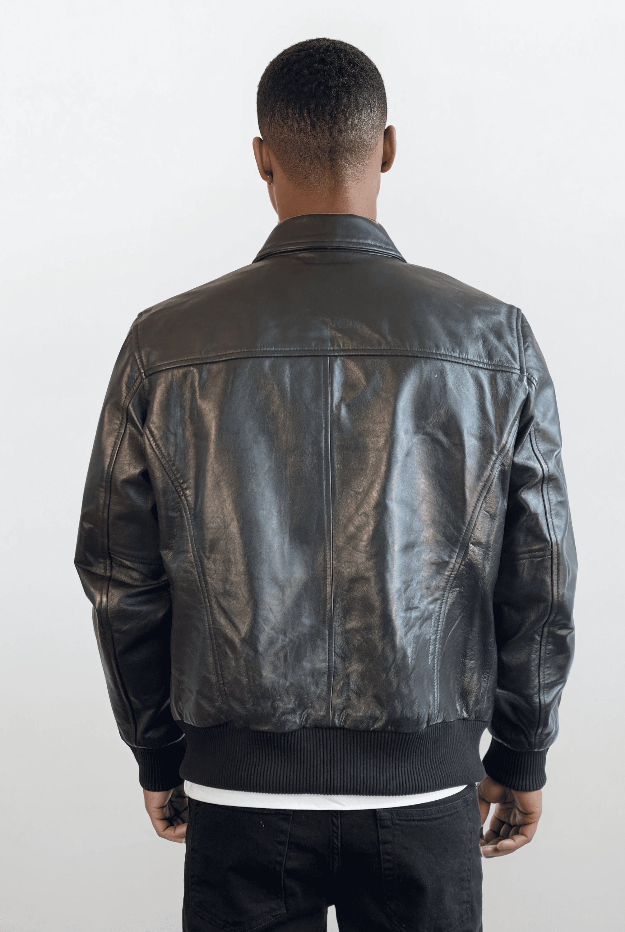 Eine Person mit kurzem Haar trägt die trueprodigy Herren Lederjacke aus Schafsleder in Schwarz im klassischen Blouson-Schnitt, dazu schwarze Hose und weißes Shirt. Der Hintergrund ist schlicht und hell.