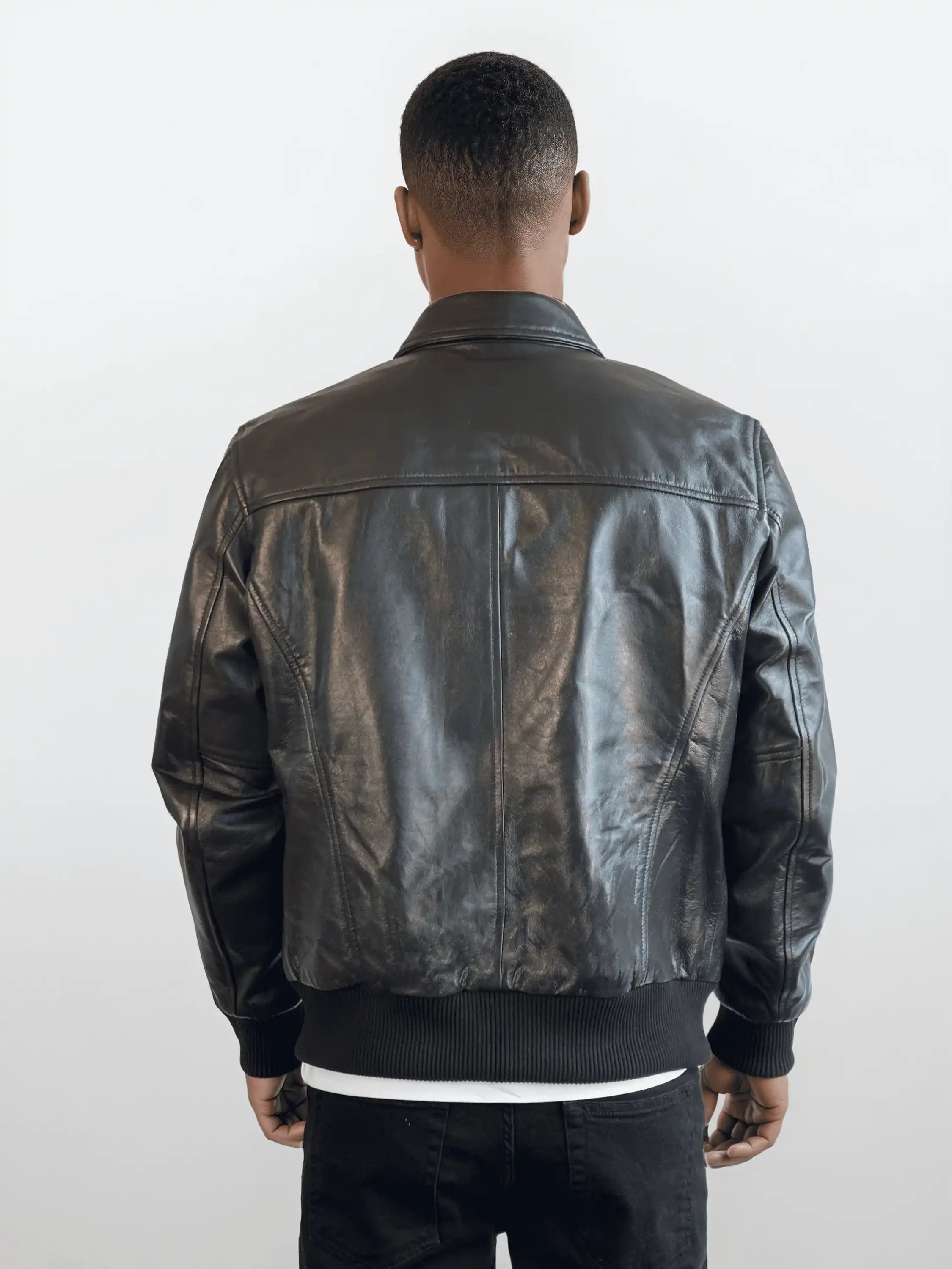 Eine Person mit kurzem Haar trägt die trueprodigy Herren Lederjacke aus Schafsleder in Schwarz im klassischen Blouson-Schnitt, dazu schwarze Hose und weißes Shirt. Der Hintergrund ist schlicht und hell.