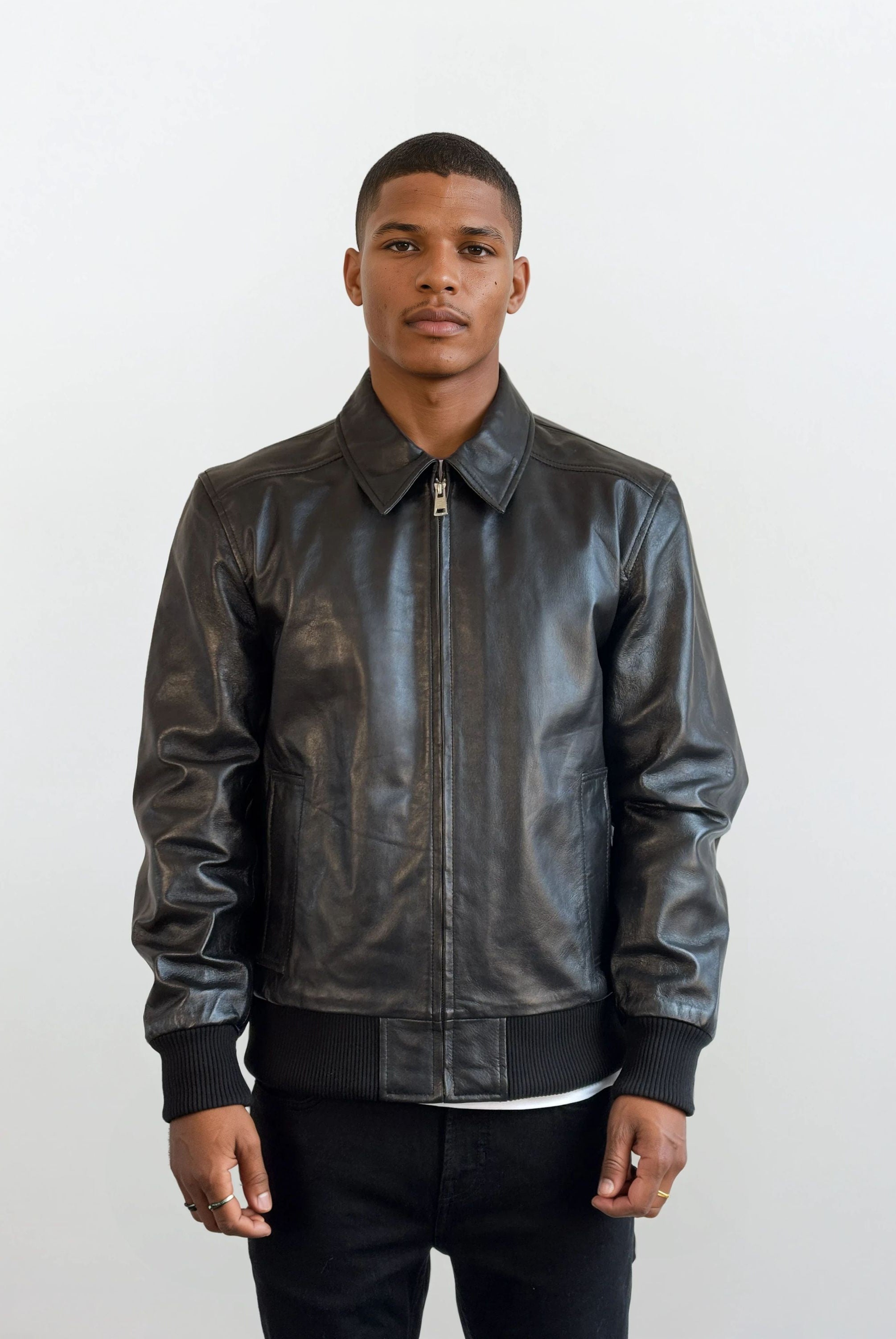 Ein Mann trägt die trueprodigy Herren Lederjacke aus Schafsleder in Schwarz im klassischen Blouson-Schnitt, kombiniert mit weißem Shirt und schwarzen Hosen, vor hellem Hintergrund. Er blickt neutral nach vorne, die Hände seitlich entspannt.