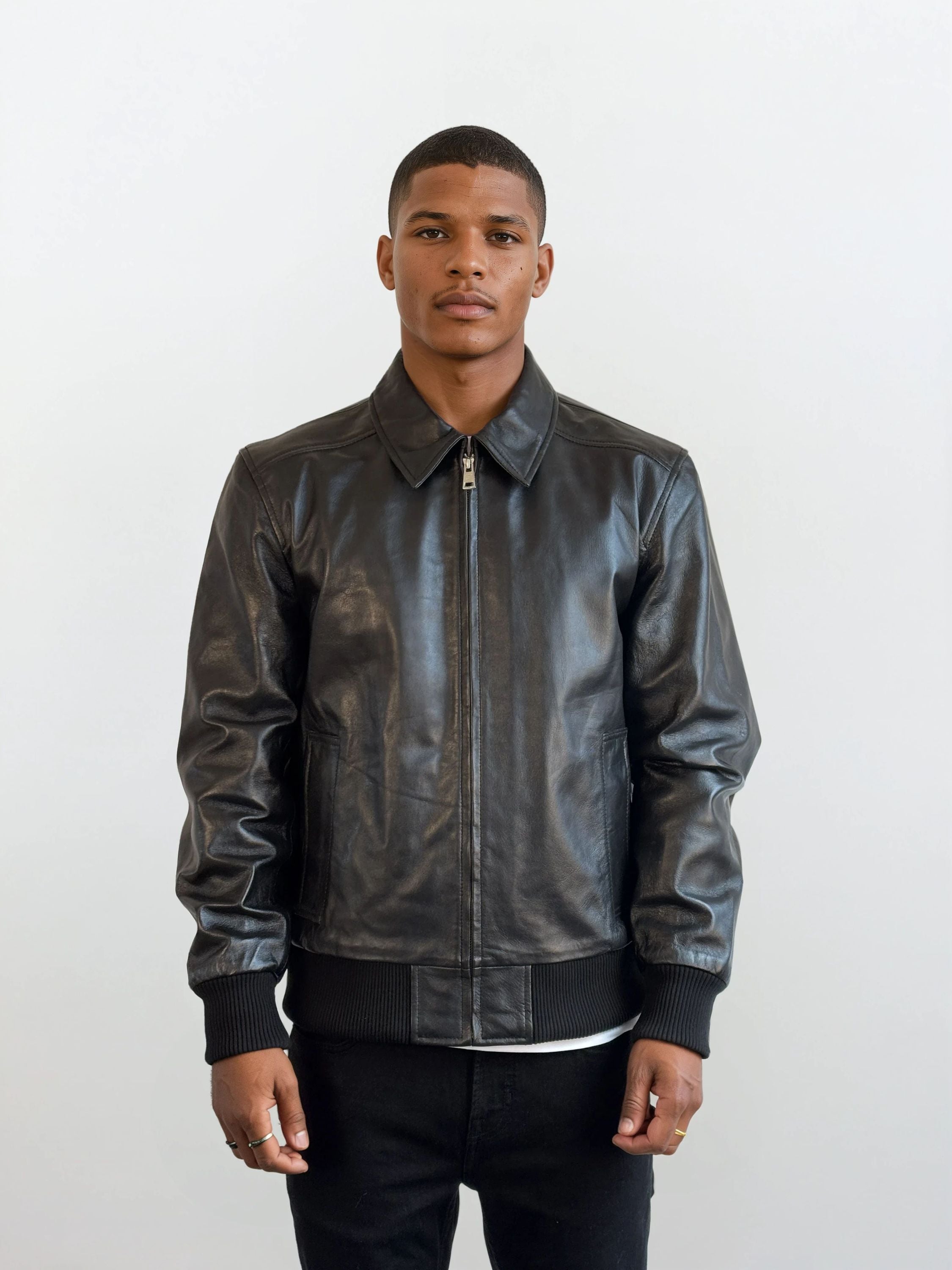 Ein Mann trägt die trueprodigy Herren Lederjacke aus Schafsleder in Schwarz im klassischen Blouson-Schnitt, kombiniert mit weißem Shirt und schwarzen Hosen, vor hellem Hintergrund. Er blickt neutral nach vorne, die Hände seitlich entspannt.