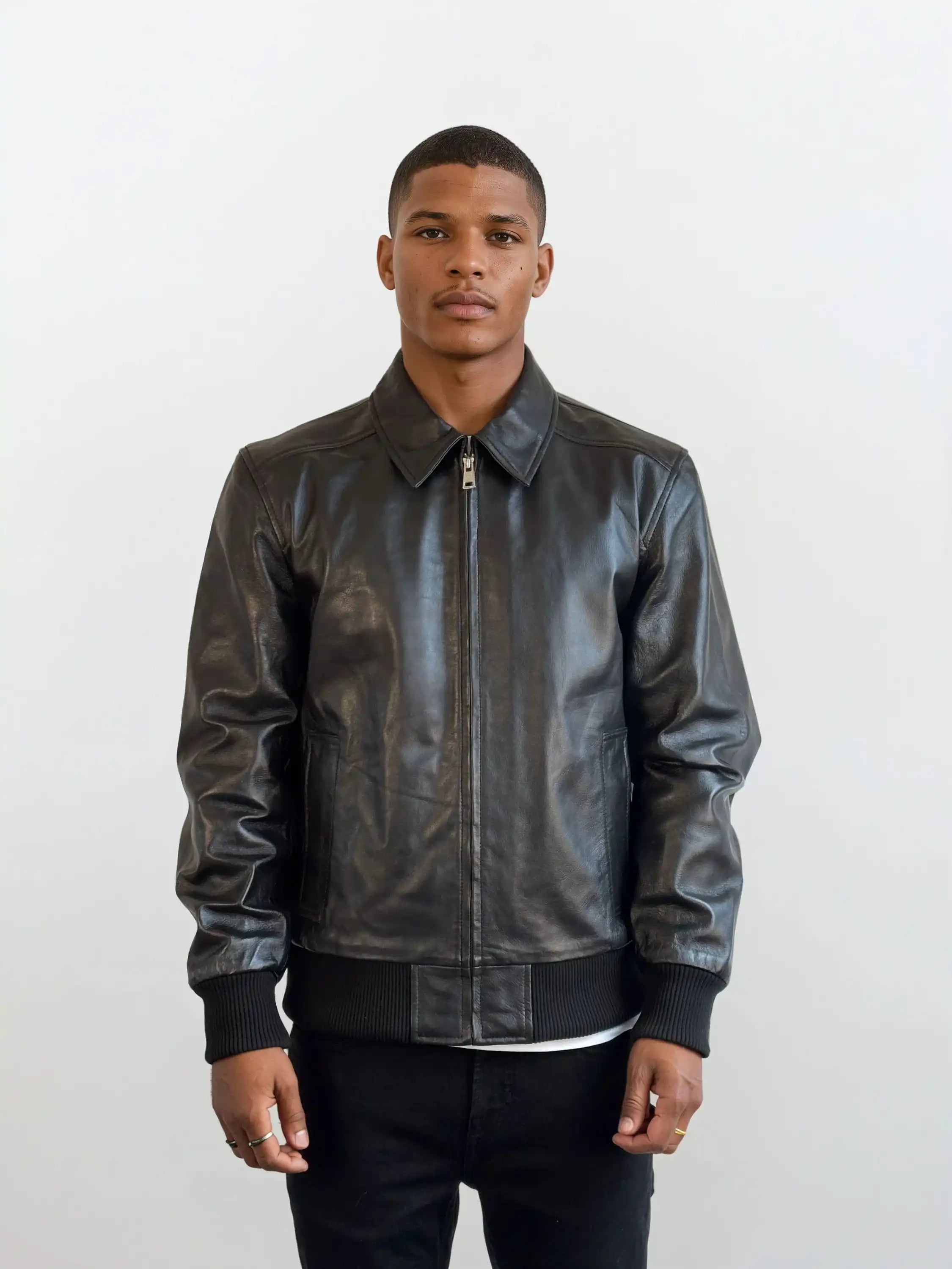 Ein Mann trägt die trueprodigy Herren Lederjacke aus Schafsleder in Schwarz im klassischen Blouson-Schnitt, kombiniert mit weißem Shirt und schwarzen Hosen, vor hellem Hintergrund. Er blickt neutral nach vorne, die Hände seitlich entspannt.