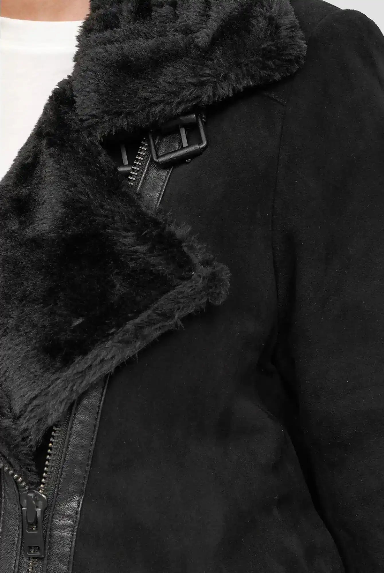 Nahaufnahme einer Person, die die trueprodigy Aloy Wilderlederjacke mit Gürtel in Schwarz mit Kunstfellfutter, sichtbarem Reißverschluss und Kragenschnalle über einem weißen Hemd trägt.