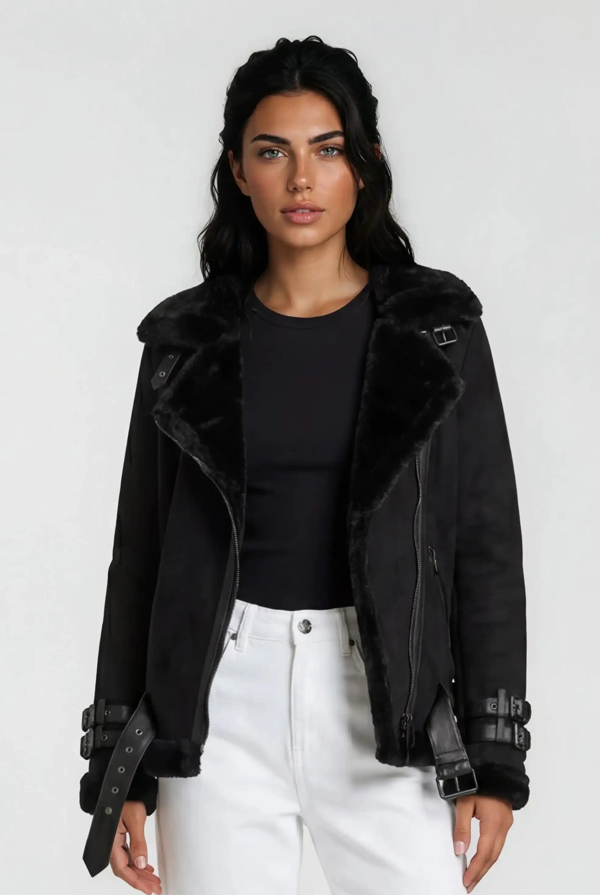 Eine Person mit langen dunklen Haaren trägt eine Trueprodigy Wilderlederjacke mit Gürtel über einem schwarzen Oberteil und einer weißen Hose mit hoher Taille vor einem schlichten hellen Hintergrund.