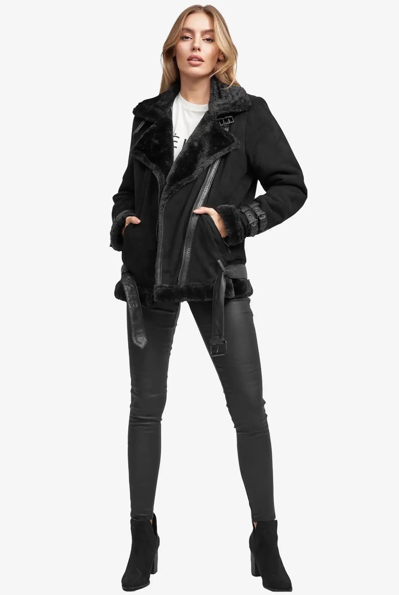 Eine Person steht vor der Kamera und trägt eine echte Aloy Wilderlederjacke mit Gürtel, eine schwarze Hose in Lederoptik, schwarze Stiefeletten und darunter ein weißes Oberteil. Der Hintergrund ist einfarbig weiß.