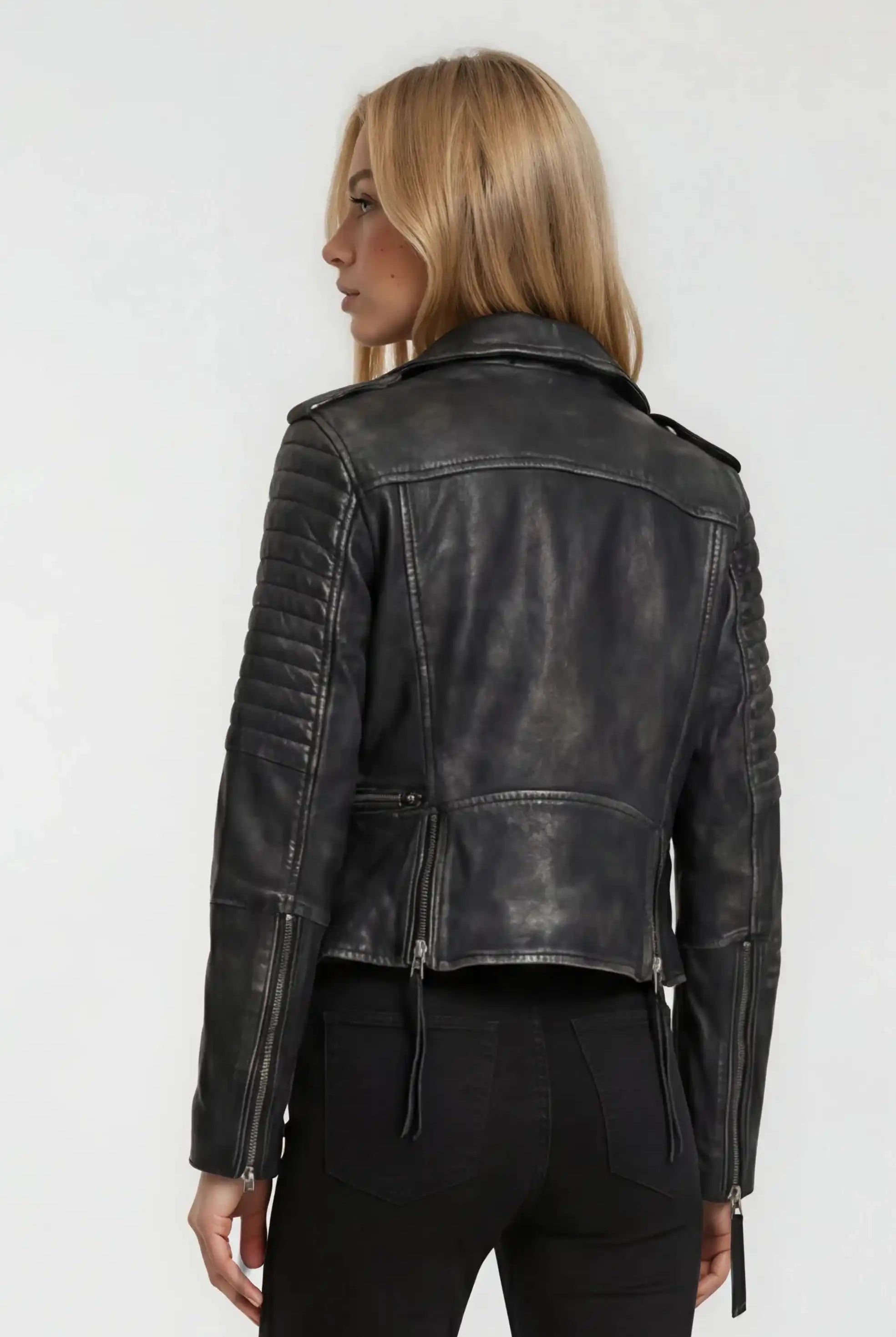 Eine Person mit langem, glattem blondem Haar wird von hinten gezeigt und trägt eine schwarze Bikerlederjacke Vintage Optik von trueprodigy und eine schwarze Jeans vor einem schlichten, hellen Hintergrund.