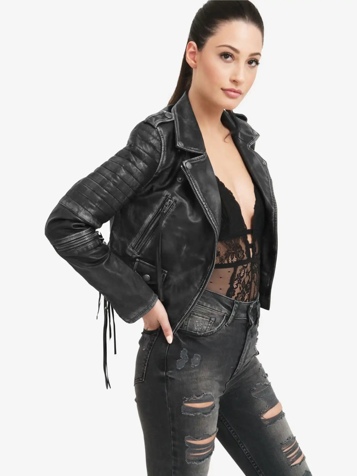 Eine Frau trägt die trueprodigy Avril Bikerlederjacke Vintage Optik mit einem schwarzen Spitzentop und einer schwarzen Jeans im Used-Look und steht mit einer Hand an der Hüfte vor einem schlichten weißen Hintergrund.