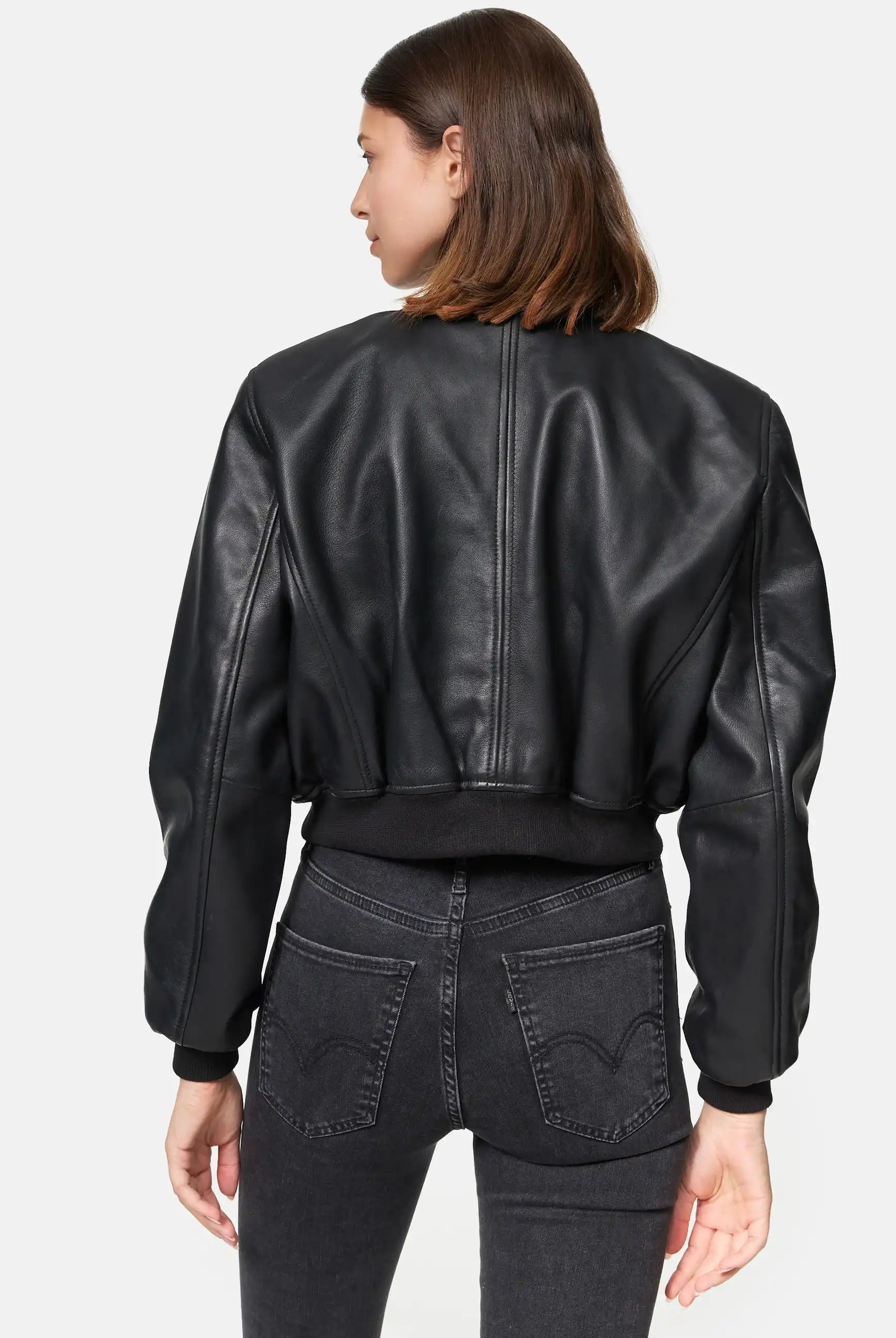 Eine Person mit glattem braunem Haar ist von hinten zu sehen. Sie trägt die trueprodigy Paola Kurze Oversized Lederjacke und eine schwarze Jeans mit hoher Taille vor einem schlichten weißen Hintergrund.
