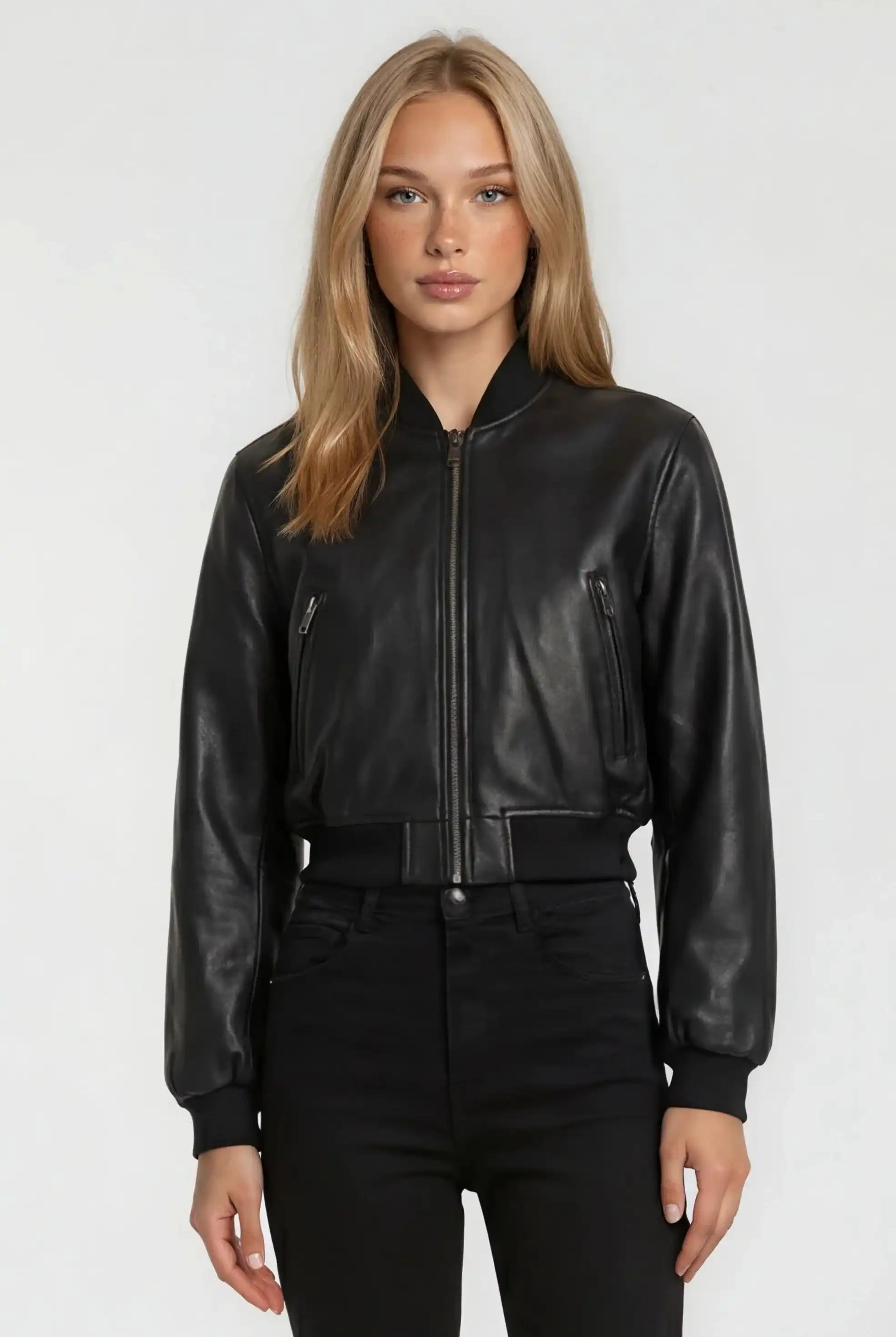 Eine Person mit langen blonden Haaren blickt nach vorne und trägt eine trueprodigy Kurze Oversized Lederjacke und eine schwarze Hose vor einem schlichten hellen Hintergrund.