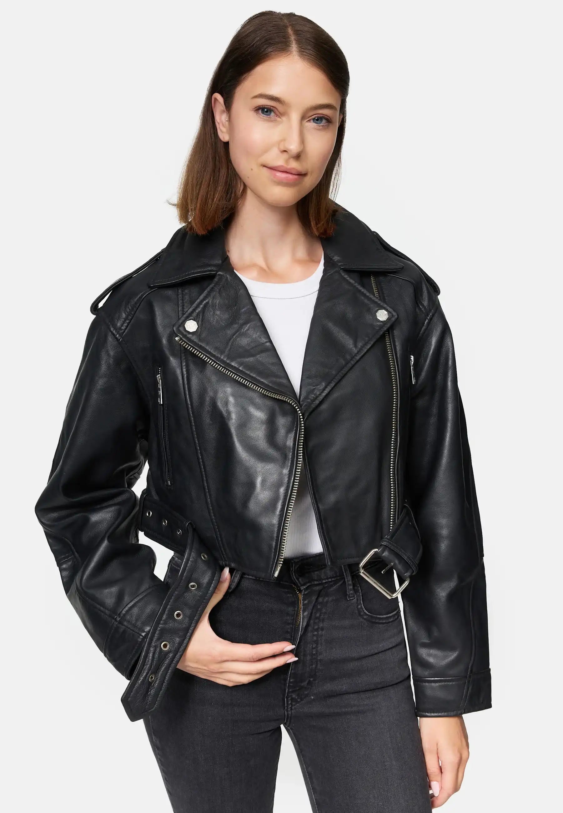 Eine Frau mit glattem braunem Haar trägt die Rosa Kurze Bomber-Lederjacke von trueprodigy über einem weißen Hemd und schwarzen Jeans. Sie steht vor einem schlichten weißen Hintergrund, eine Hand in der Tasche, die andere hält ihre Jacke.