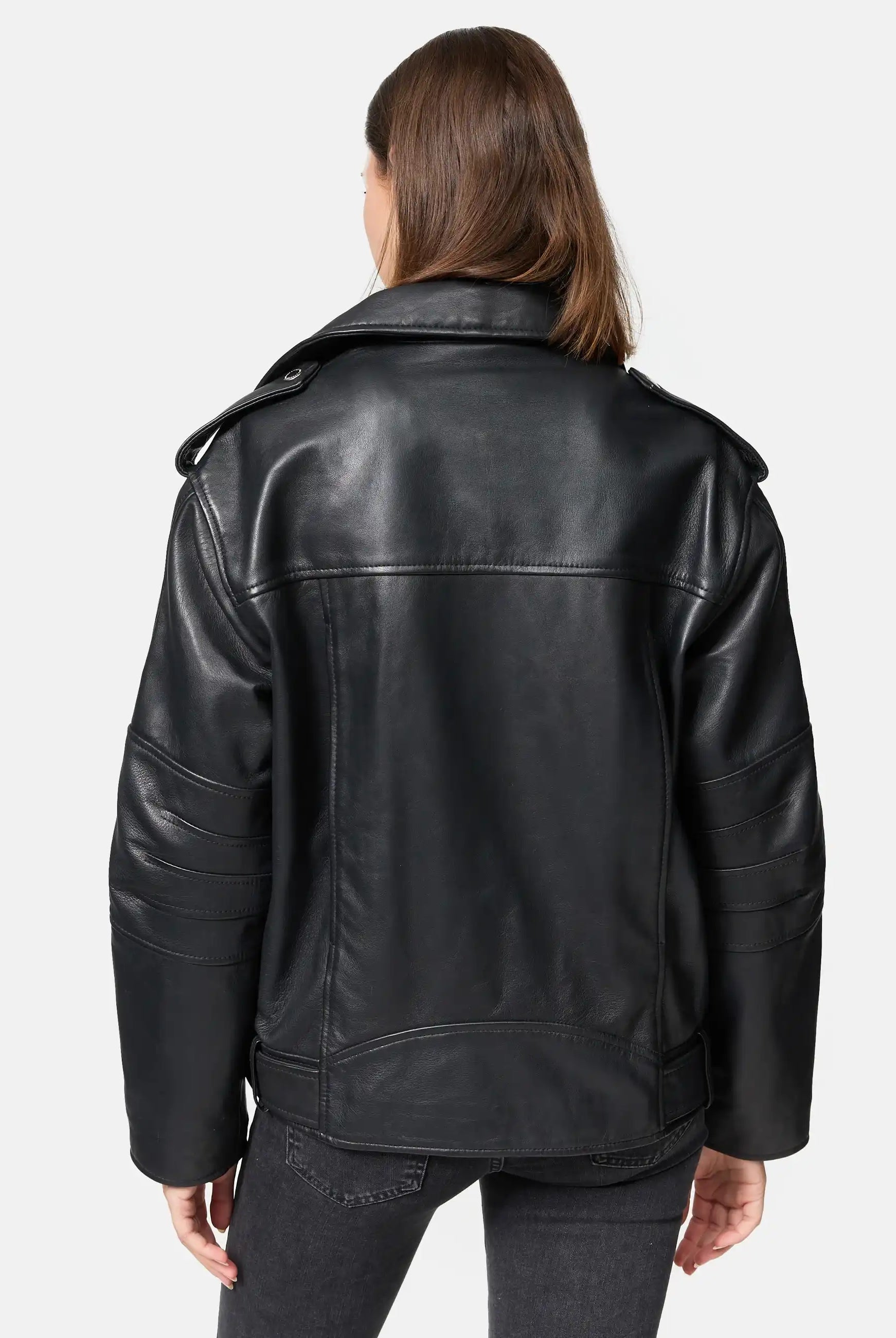 Eine Person mit glattem braunem Haar wird von hinten gezeigt, die eine Trueprodigy Dua Lange übergroße Bikerlederjacke mit breiten Schultern und dunkelgraue Jeans vor einem schlichten hellen Hintergrund trägt.