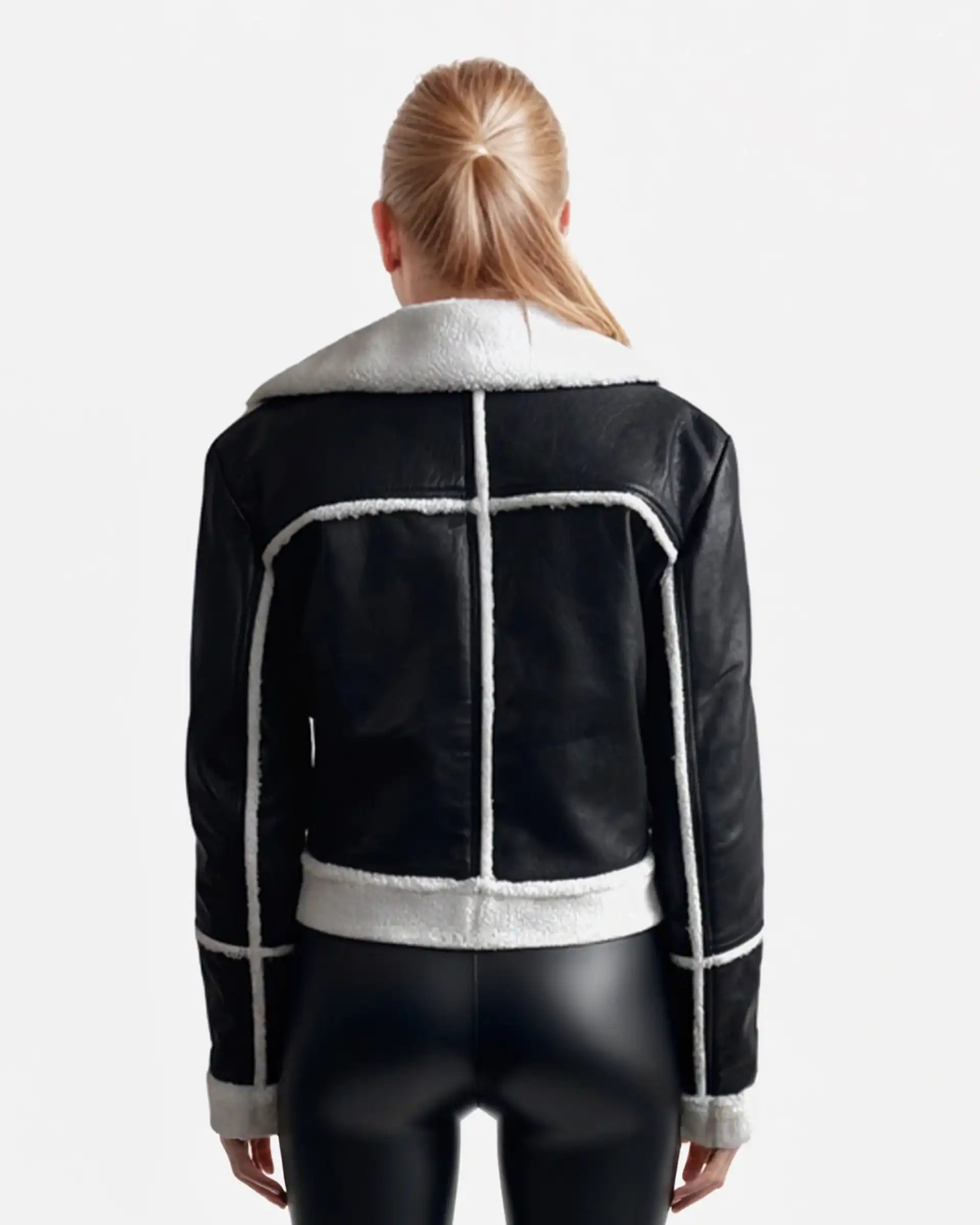 Eine Person mit langen blonden Haaren, von hinten gesehen, trägt eine trueprodigy Damen-Lederjacke mit weißen Teddy-Kontrasten & asymmetrischem Zipper in schwarz und taillierter Hose, stehend vor einem schlichten weißen Hintergrund.