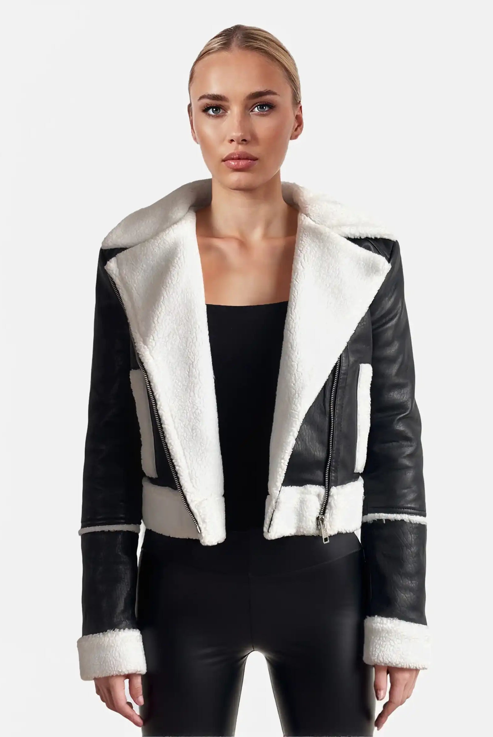 Eine Person steht mit dem Gesicht nach vorne und trägt eine trueprodigy Damen-Lederjacke mit weißen Teddy-Kontrasten & asymmetrischem Reißverschluss über einem schwarzen Oberteil und einer Hose vor einem schlichten hellen Hintergrund.