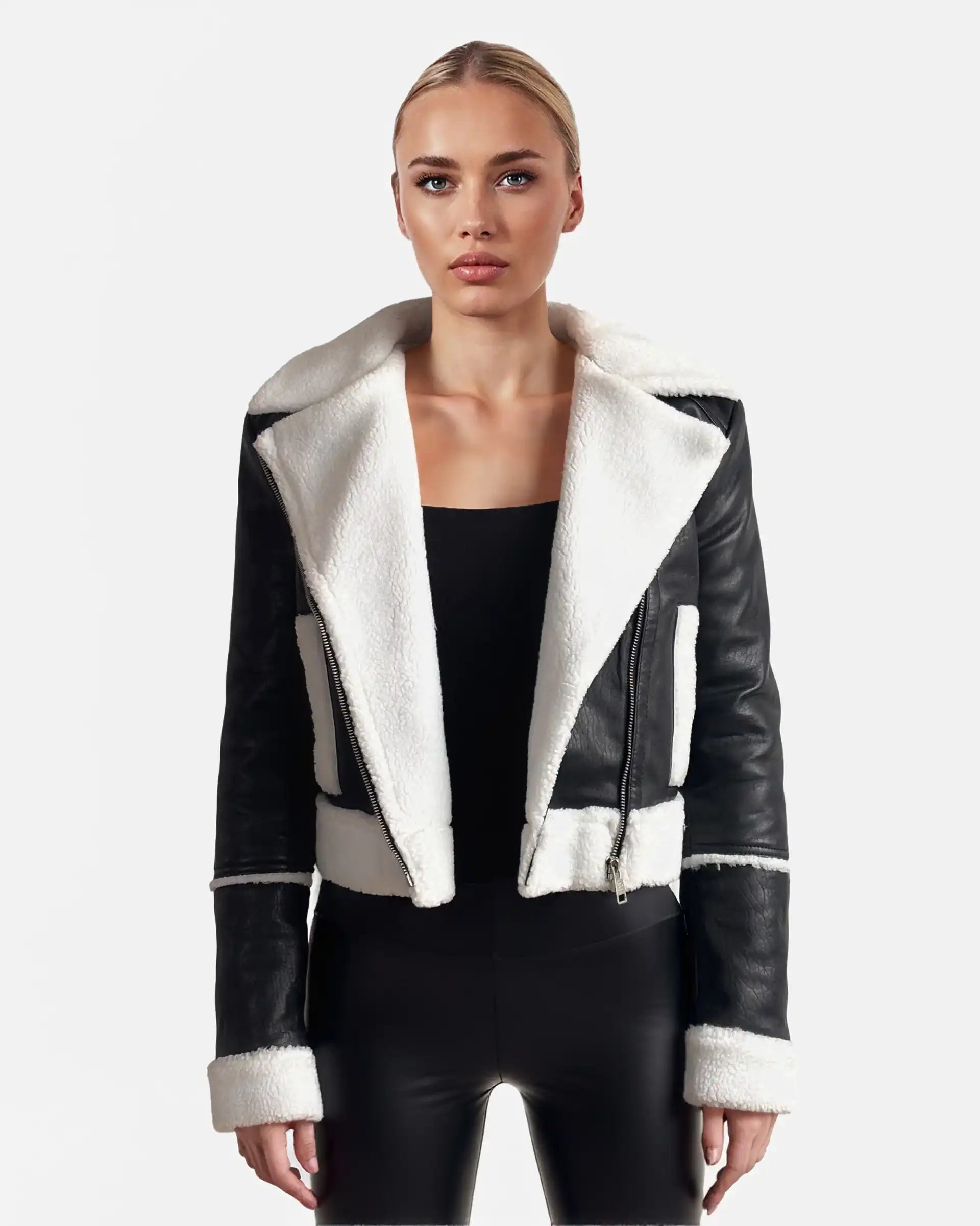 Eine Person steht mit dem Gesicht nach vorne und trägt eine trueprodigy Damen-Lederjacke mit weißen Teddy-Kontrasten & asymmetrischem Reißverschluss über einem schwarzen Oberteil und einer Hose vor einem schlichten hellen Hintergrund.