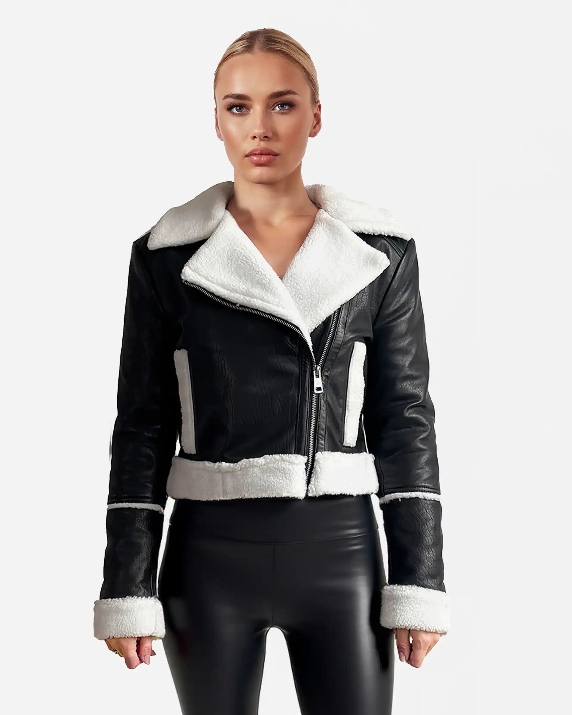 Eine Frau schaut nach vorne in einer trueprodigy Damen-Lederjacke mit weißen Teddy-Kontrasten & asymmetrischem Reißverschluss in Schwarz, kombiniert mit glänzenden schwarzen Hosen vor hellem, schlichtem Hintergrund.