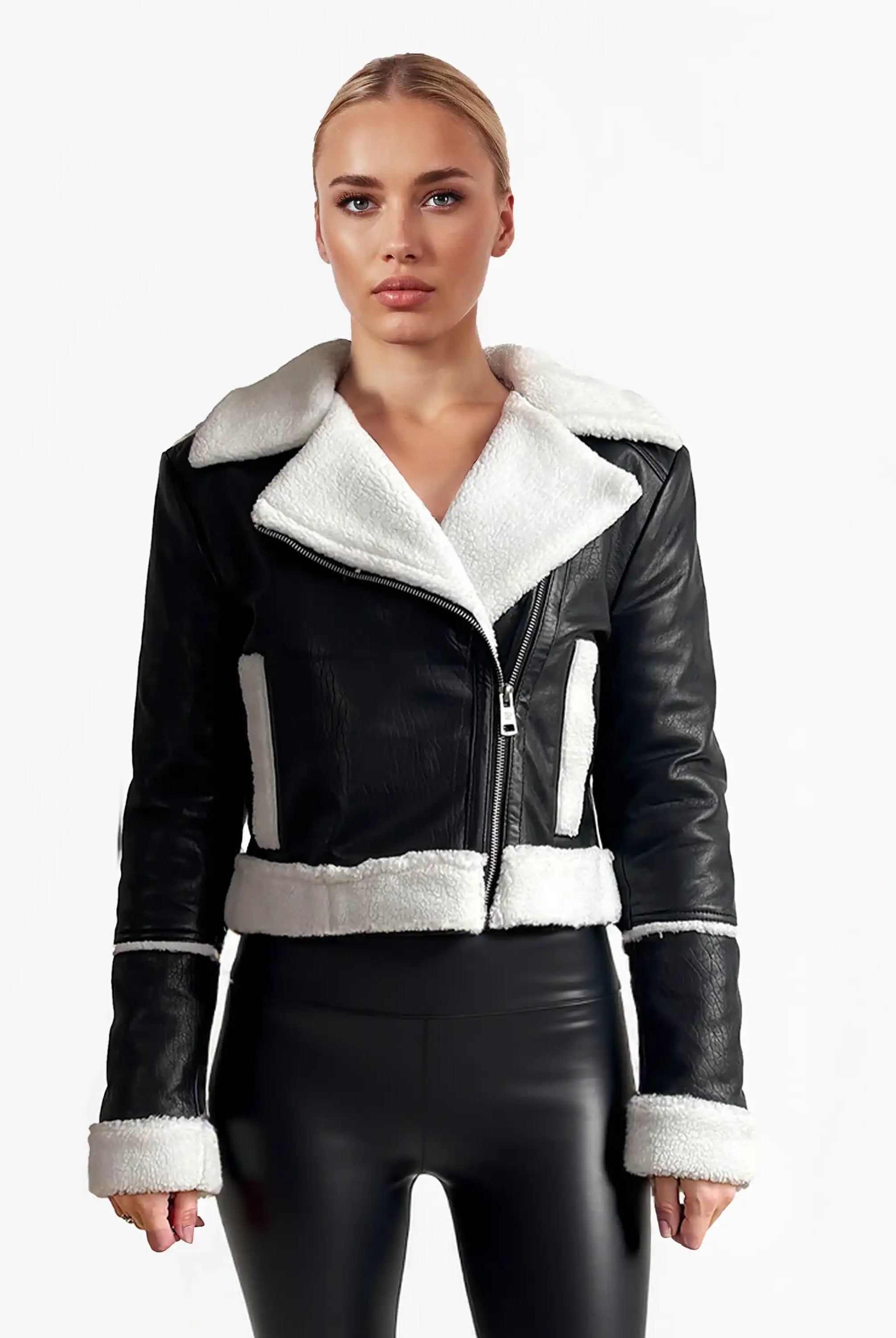 Eine Frau blickt nach vorne in einer trueprodigy Damen-Lederjacke mit weißen Teddy-Kontrasten & asymmetrischem Reißverschluss und schwarzen glänzenden Leggings vor einem schlichten weißen Hintergrund.