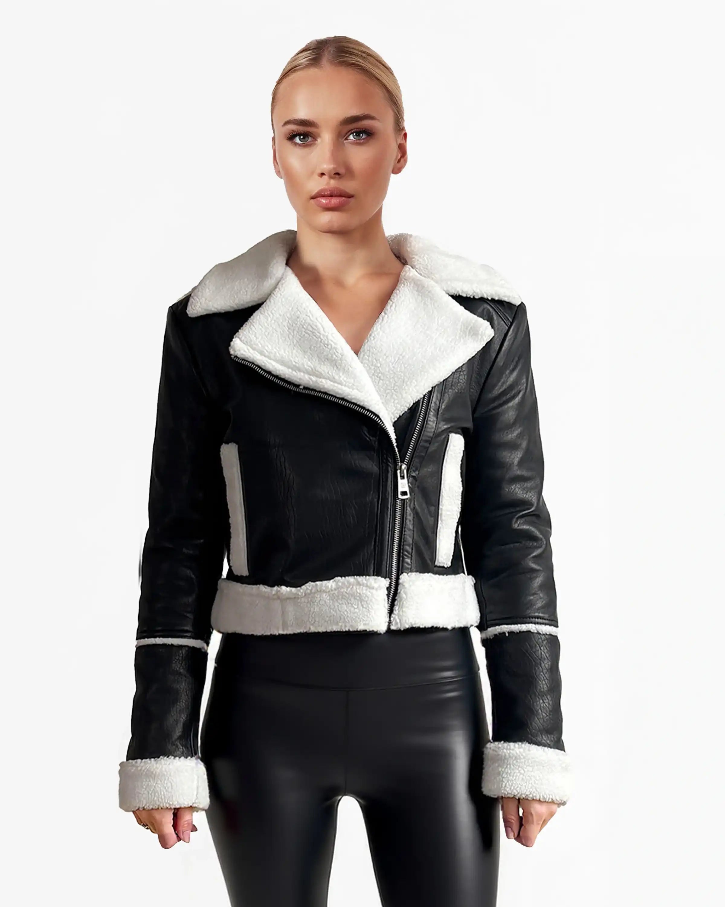 Eine Frau blickt nach vorne in einer trueprodigy Damen-Lederjacke mit weißen Teddy-Kontrasten & asymmetrischem Reißverschluss und schwarzen glänzenden Leggings vor einem schlichten weißen Hintergrund.