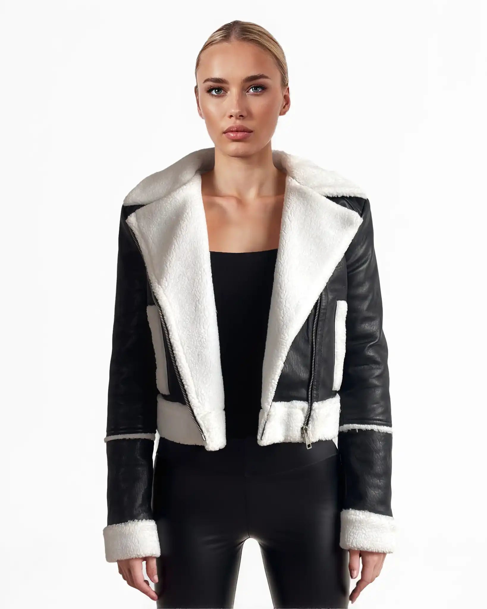 Eine Frau blickt nach vorne und trägt die trueprodigy Damen-Lederjacke mit weißen Teddy-Kontrasten & asymmetrischem Reißverschluss über einem schwarzen Oberteil und einer Hose. Die Jacke hat einen breiten weißen Kragen, Manschetten und Besätze. Der Hintergrund ist einfarbig weiß.