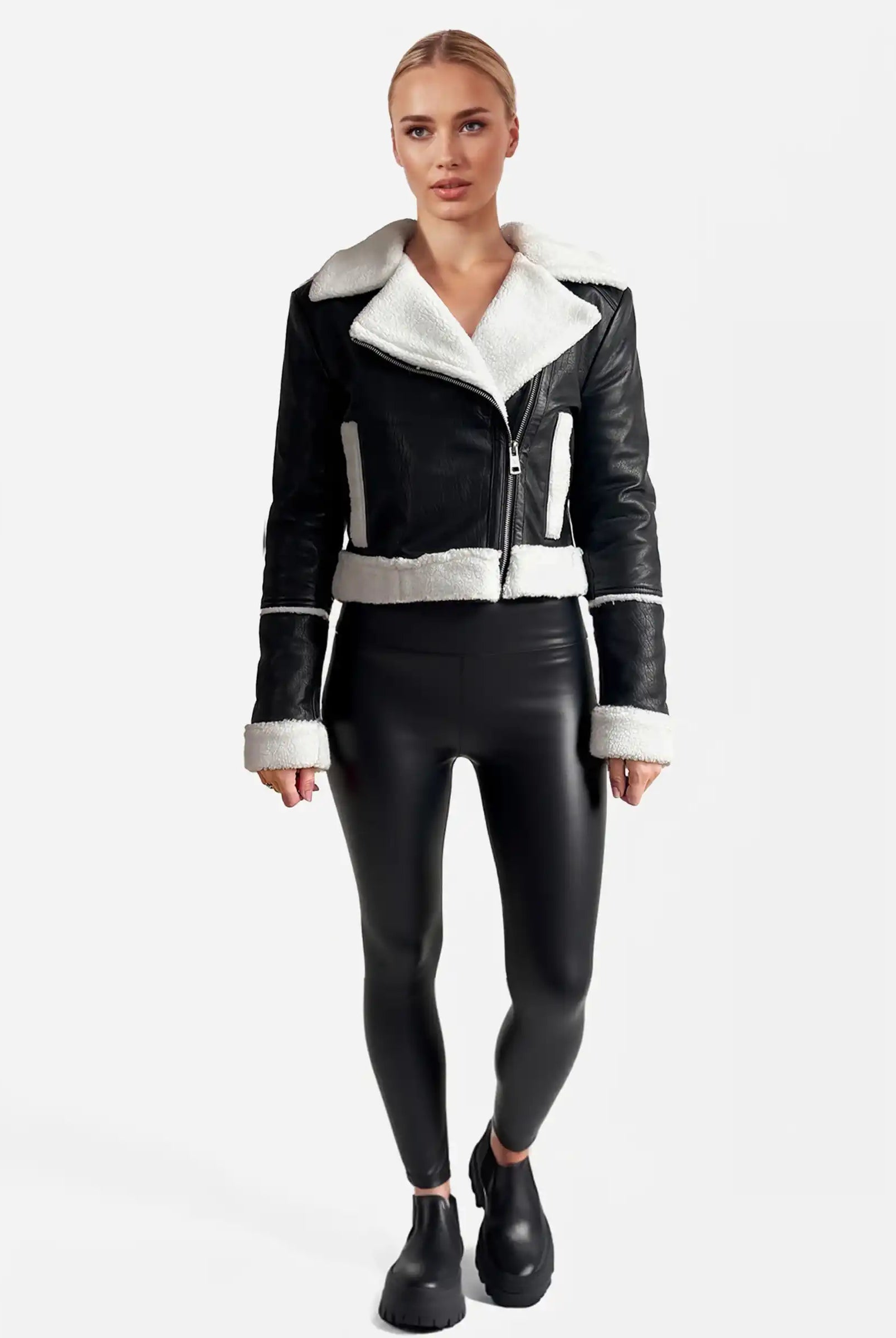 Eine Person steht mit dem Gesicht nach vorne und trägt eine trueprodigy Damen-Lederjacke mit weißen Teddy-Kontrasten & asymmetrischem Reißverschluss, eine schwarze taillierte Hose und schwarze Slipper vor einem schlichten weißen Hintergrund.