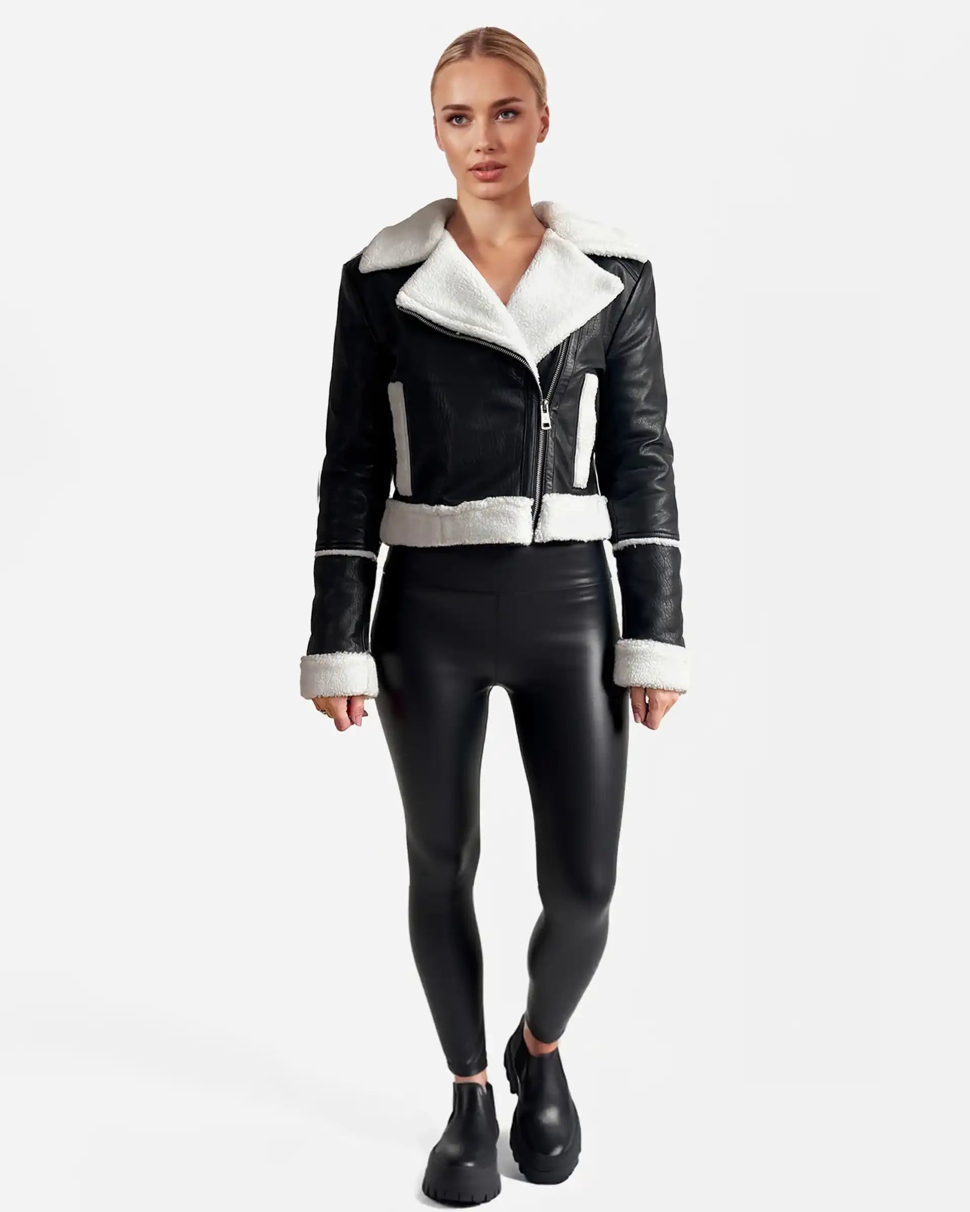 Eine Person steht mit dem Gesicht nach vorne und trägt eine trueprodigy Damen-Lederjacke mit weißen Teddy-Kontrasten & asymmetrischem Reißverschluss, eine schwarze taillierte Hose und schwarze Slipper vor einem schlichten weißen Hintergrund.