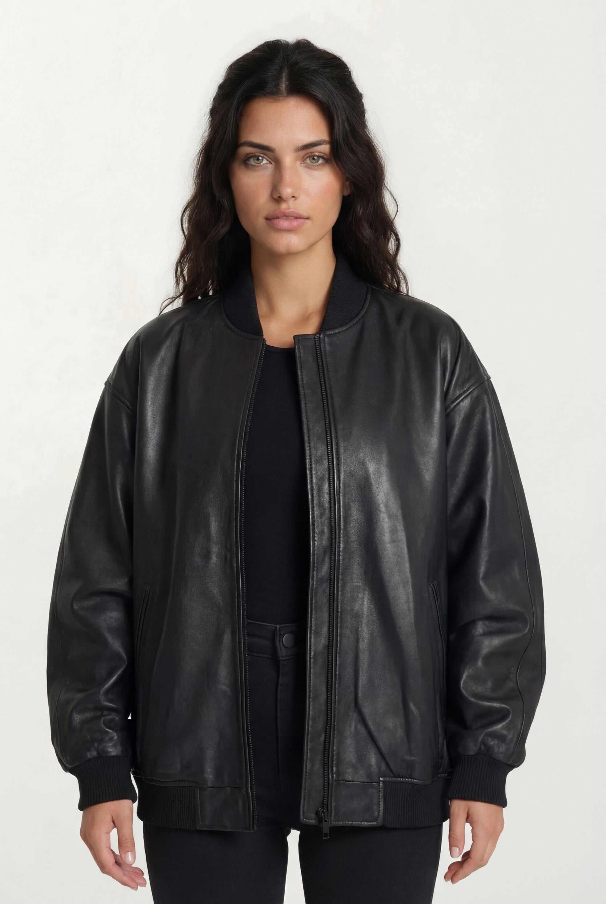 Eine Frau mit langen dunklen Haaren steht mit dem Gesicht nach vorne und trägt eine trueprodigy Oversize Bomber Lederjacke Damen "Selina" über einem schwarzen Oberteil und einer schwarzen Hose vor einem schlichten hellen Hintergrund.