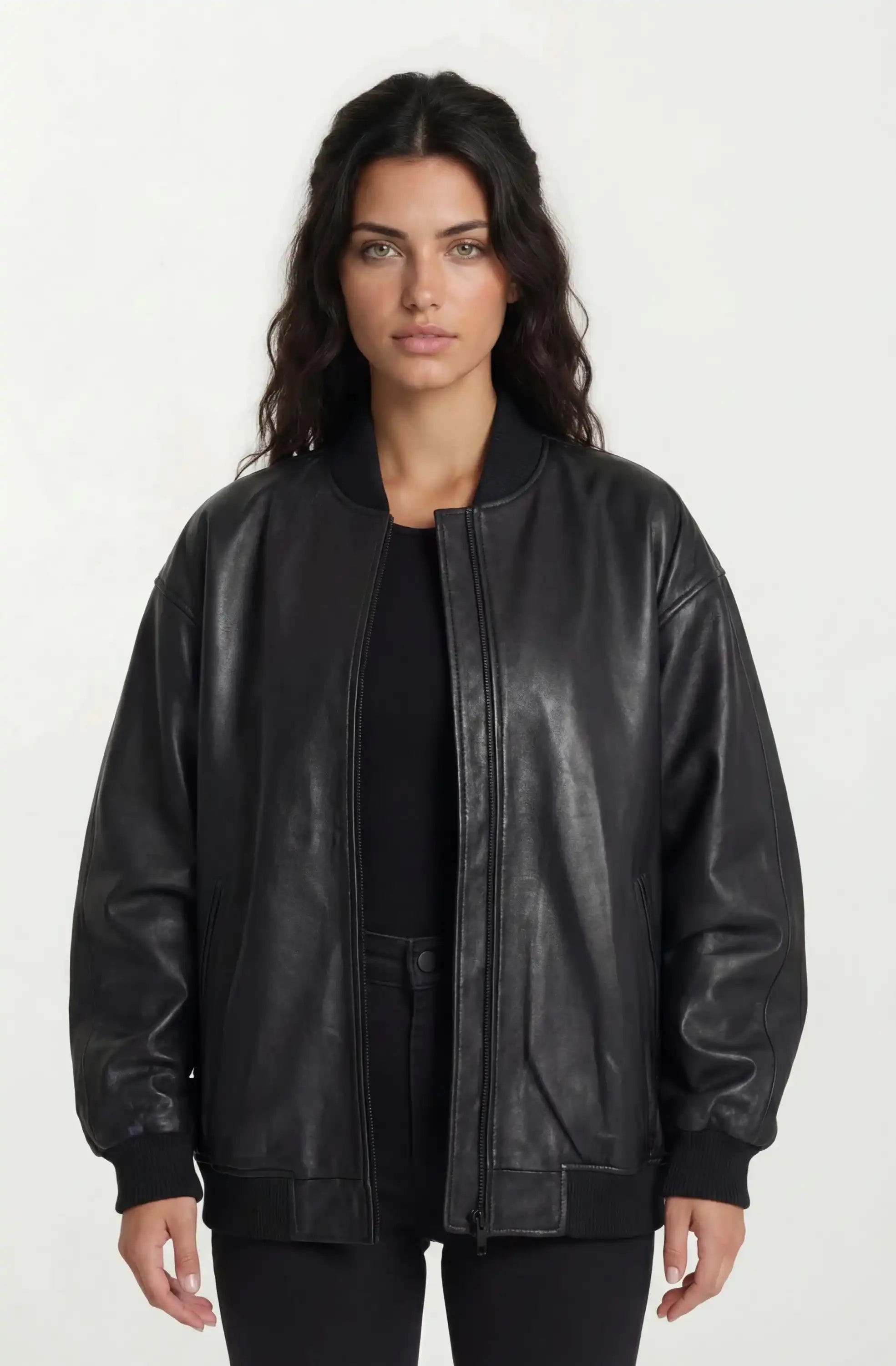 Eine Frau mit langen dunklen Haaren steht mit dem Gesicht nach vorne und trägt eine trueprodigy Oversize Bomber Lederjacke Damen "Selina" über einem schwarzen Oberteil und einer schwarzen Hose vor einem schlichten hellen Hintergrund.