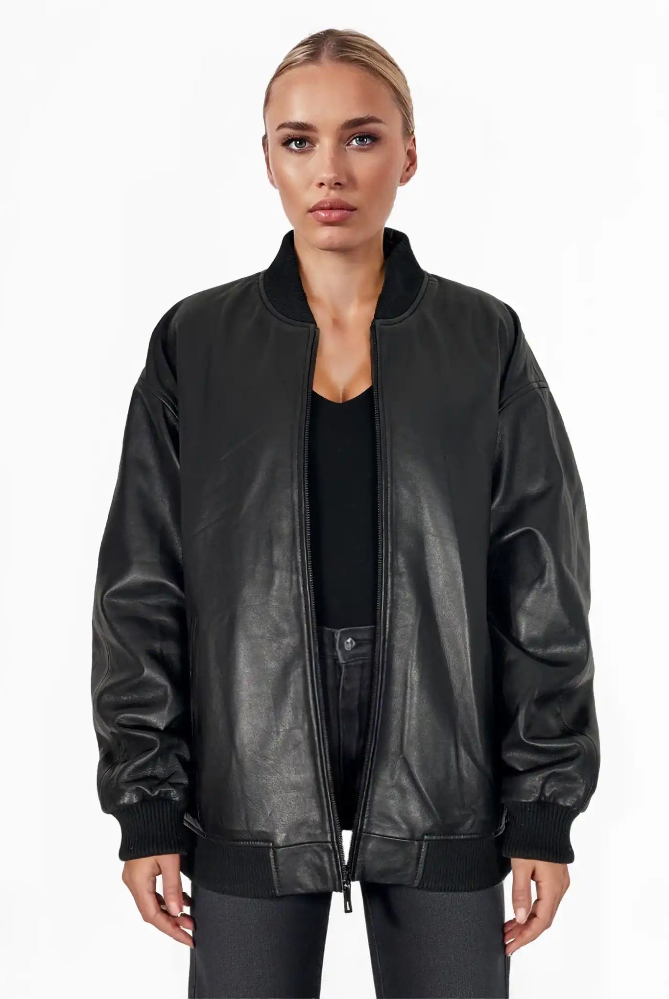 Eine Person mit zurückgebundenen blonden Haaren trägt die trueprodigy Selina Oversize-Bomberjacke aus Leder mit Rippbündchen & schwarzem Zipper über einem schwarzen Oberteil und einer dunklen Hose, stehend vor einem schlichten weißen Hintergrund.