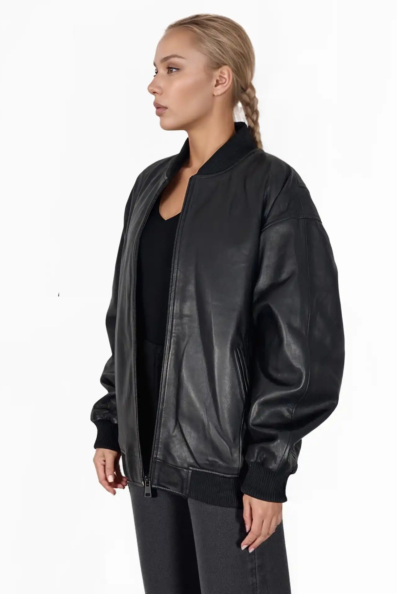 Eine blondhaarige Person mit Zopf trägt die Selina Oversize-Bomberjacke aus Leder mit Rippbündchen & schwarzem Zipper von trueprodigy über einem schwarzen Hemd und einer Hose, stehend vor einem schlichten weißen Hintergrund.