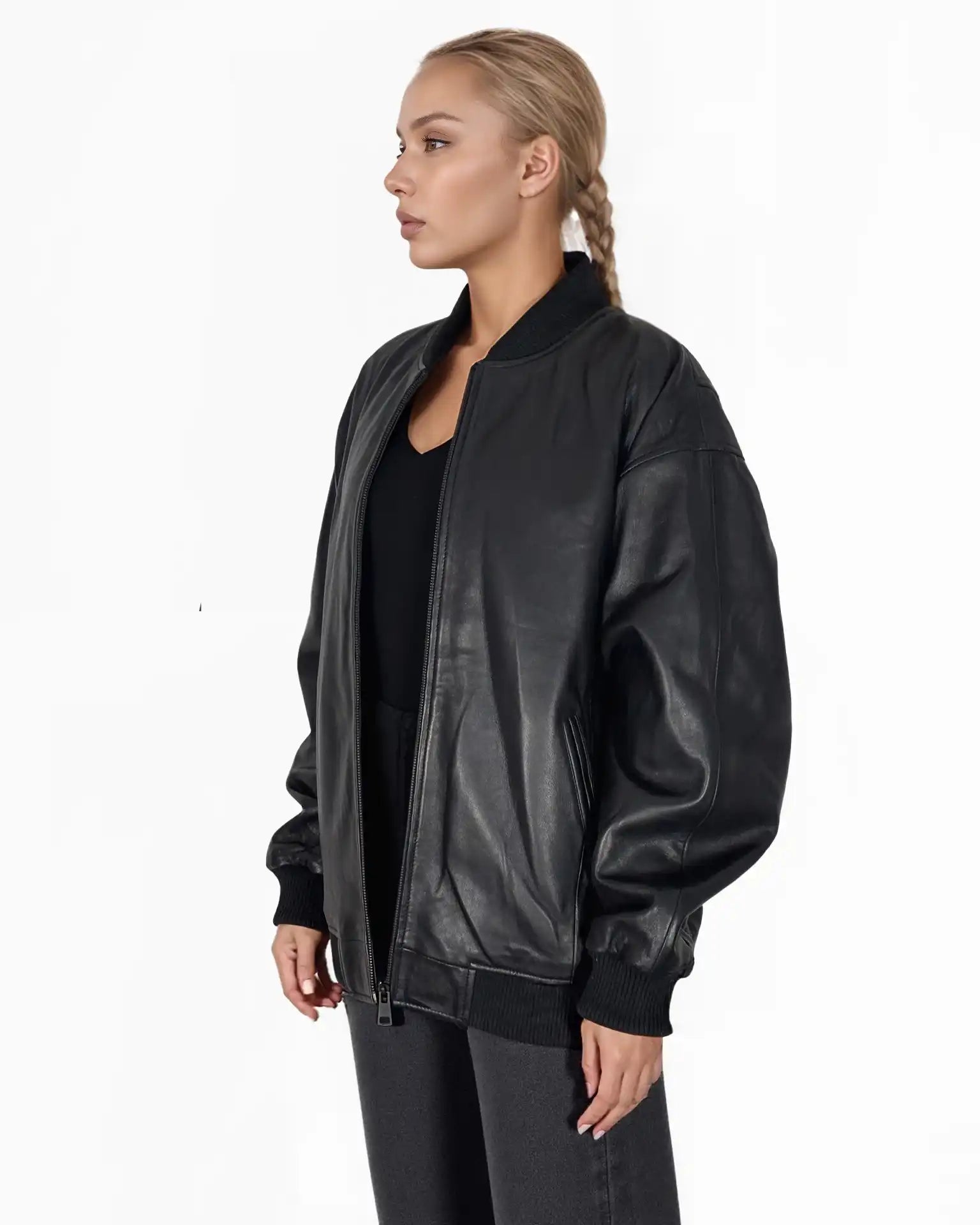 Eine blondhaarige Person mit Zopf trägt die Selina Oversize-Bomberjacke aus Leder mit Rippbündchen & schwarzem Zipper von trueprodigy über einem schwarzen Hemd und einer Hose, stehend vor einem schlichten weißen Hintergrund.