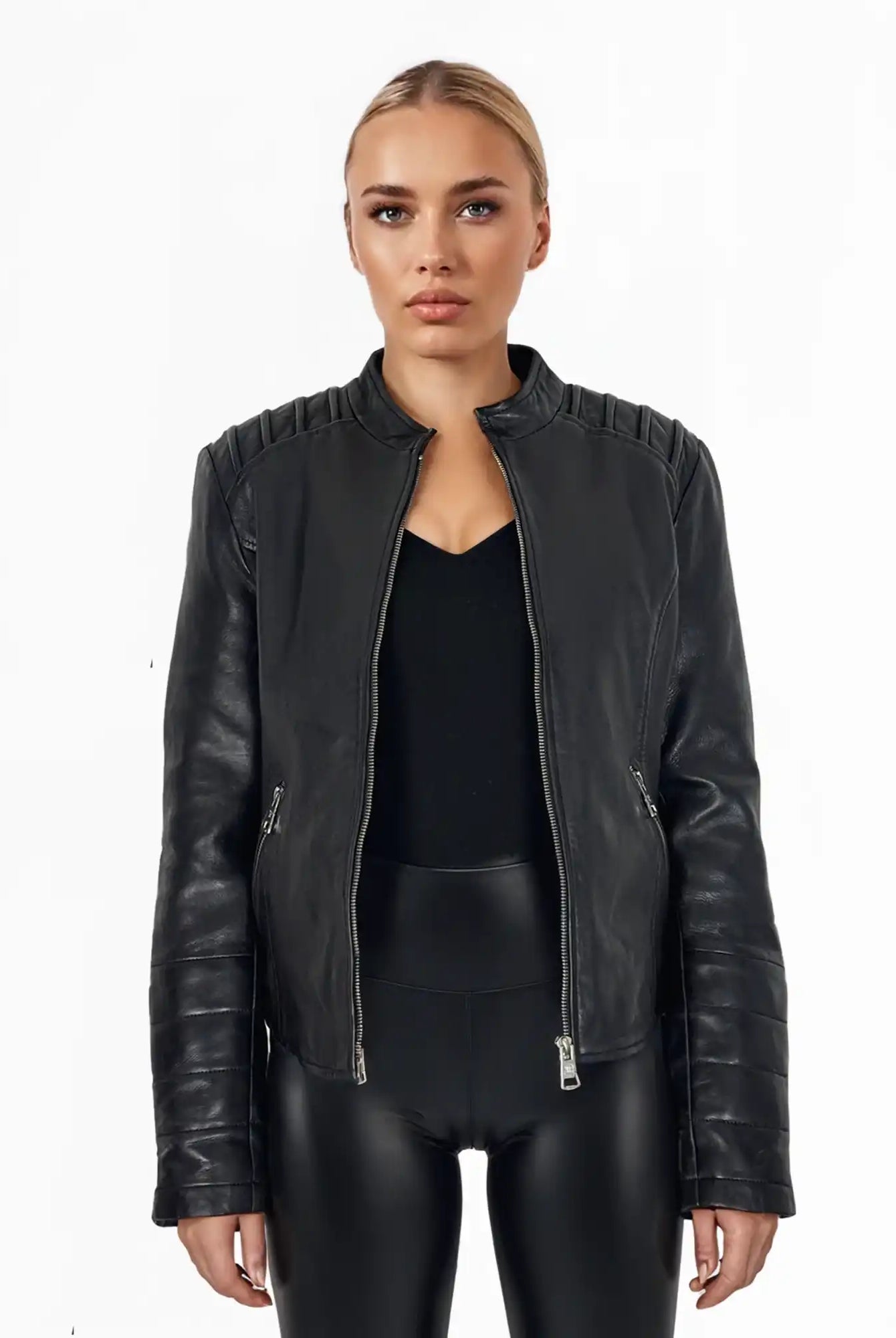 Eine Person steht vor weißem Hintergrund und trägt die Raegan taillierte Lederjacke mit Stehkragen, Steppnähten und silbernen Reißverschlüssen von trueprodigy über schwarzem Top und Hose. Ihr Ausdruck ist neutral.