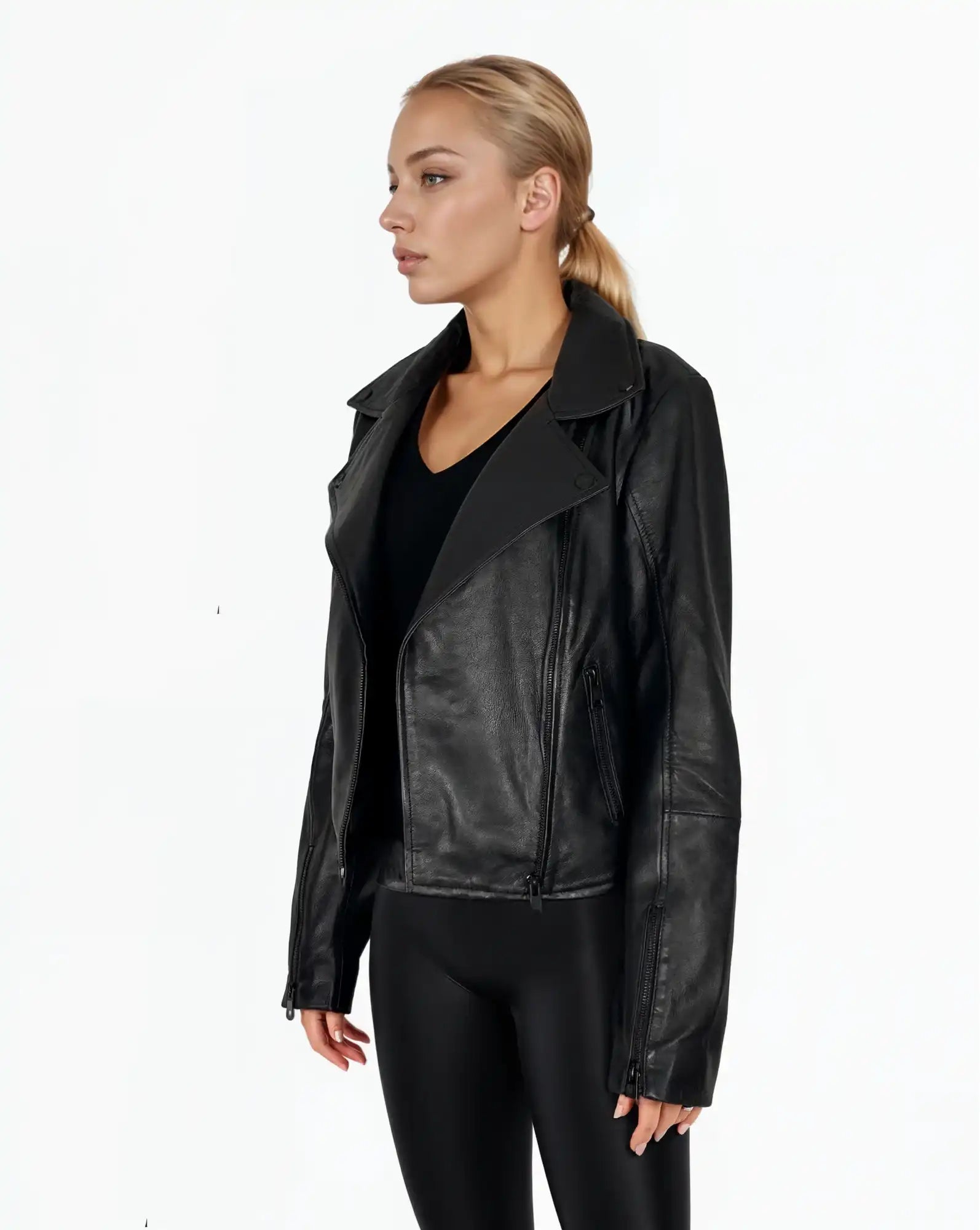 Eine Frau mit zurückgebundenen blonden Haaren trägt die trueprodigy Stella taillierte Lederjacke mit schwarzem Reißverschluss & Ärmelzipper über einem schwarzen Oberteil und Leggings. Sie steht vor einem schlichten weißen Hintergrund und schaut leicht nach links.