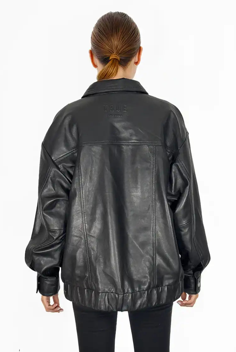 Eine Person mit zurückgebundenen braunen Haaren trägt eine Trueprodigy Nova Oversize-Lederjacke mit Gummizugsaum & Lederdetails und eine schwarze Hose und steht mit dem Rücken zur Kamera vor einem schlichten weißen Hintergrund.