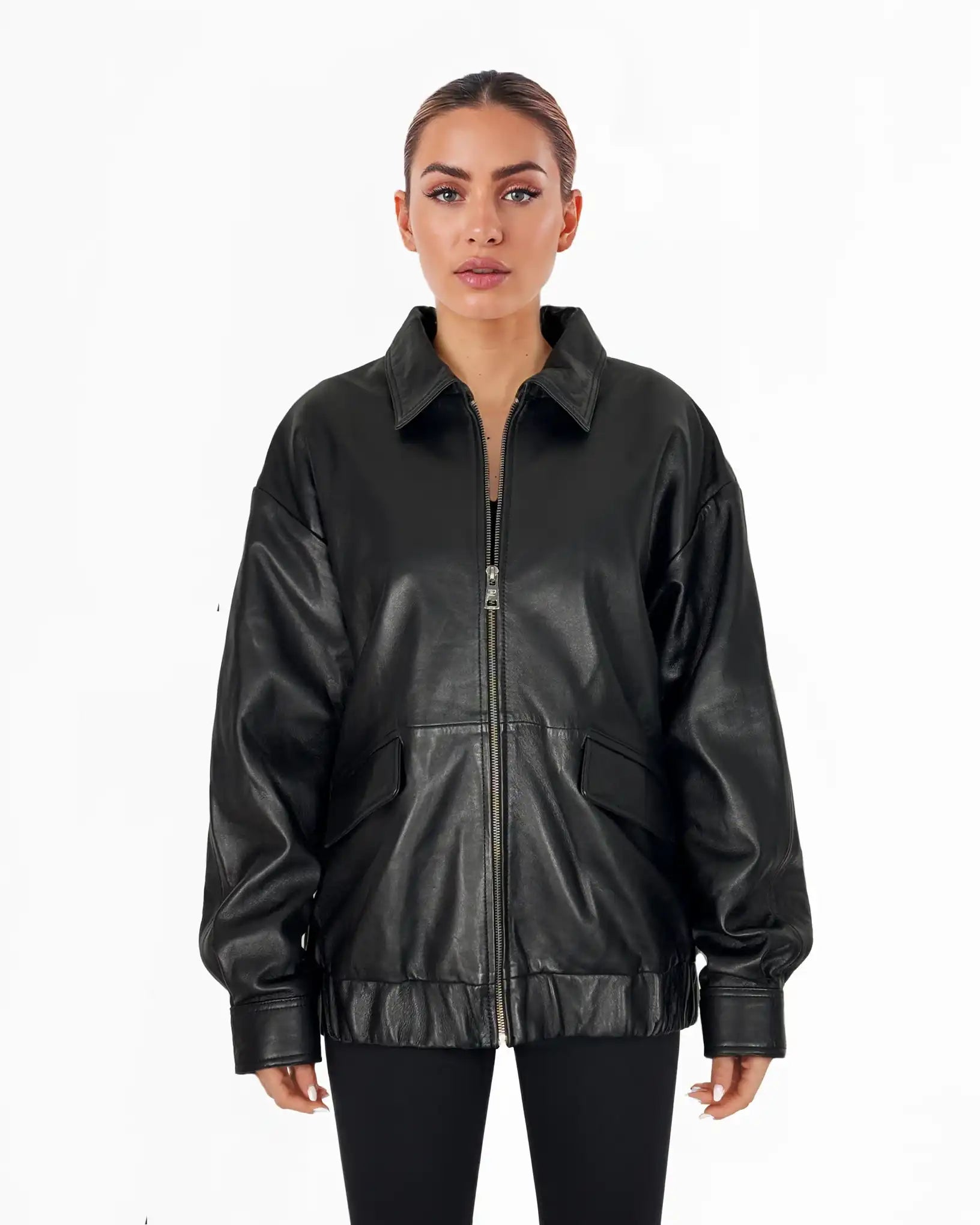 Eine Frau steht mit dem Gesicht nach vorne und trägt die trueprodigy Nova Oversize-Lederjacke mit Gummizugsaum & Lederdetails in Schwarz mit großen Vordertaschen und schwarzen Leggings vor einem schlichten weißen Hintergrund.