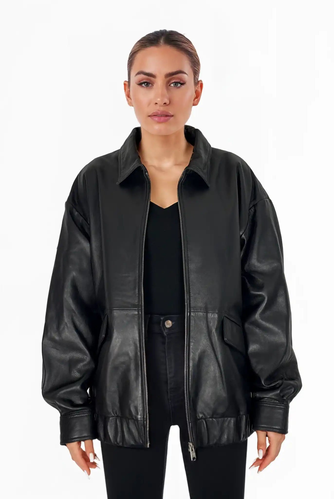 Eine Frau mit zurückgebundenem Haar trägt die trueprodigy Nova Oversize-Lederjacke mit Gummizugsaum & Lederdetails über einem schwarzen Oberteil und einer Hose. Sie steht mit neutralem Gesichtsausdruck vor einem schlichten weißen Hintergrund.