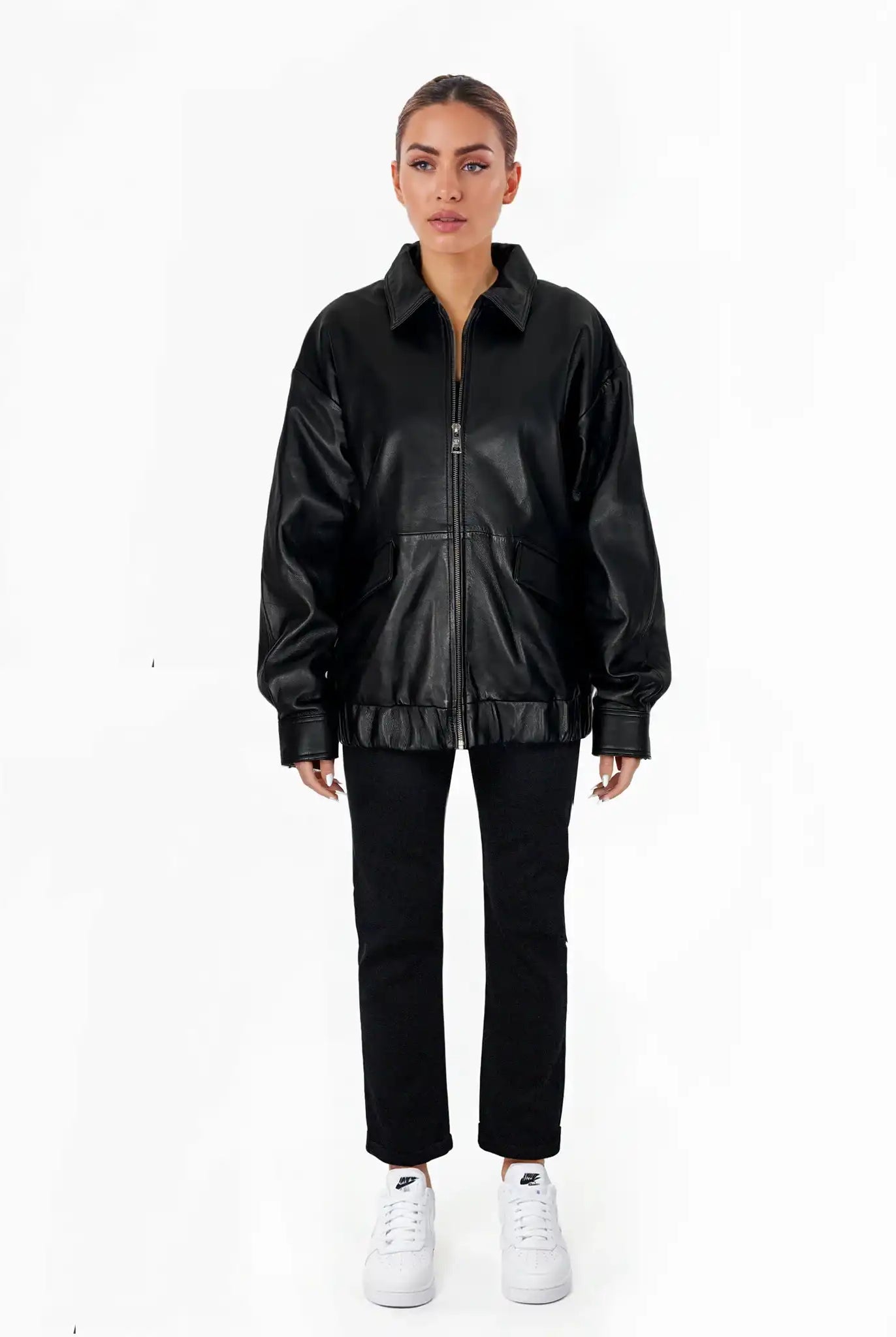 Eine Person steht mit dem Gesicht nach vorne vor einem schlichten weißen Hintergrund und trägt eine trueprodigy Nova Oversize-Lederjacke mit Gummizugsaum & Lederdetails, eine schwarze Hose und weiße Turnschuhe, wobei die Arme entspannt an der Seite liegen.