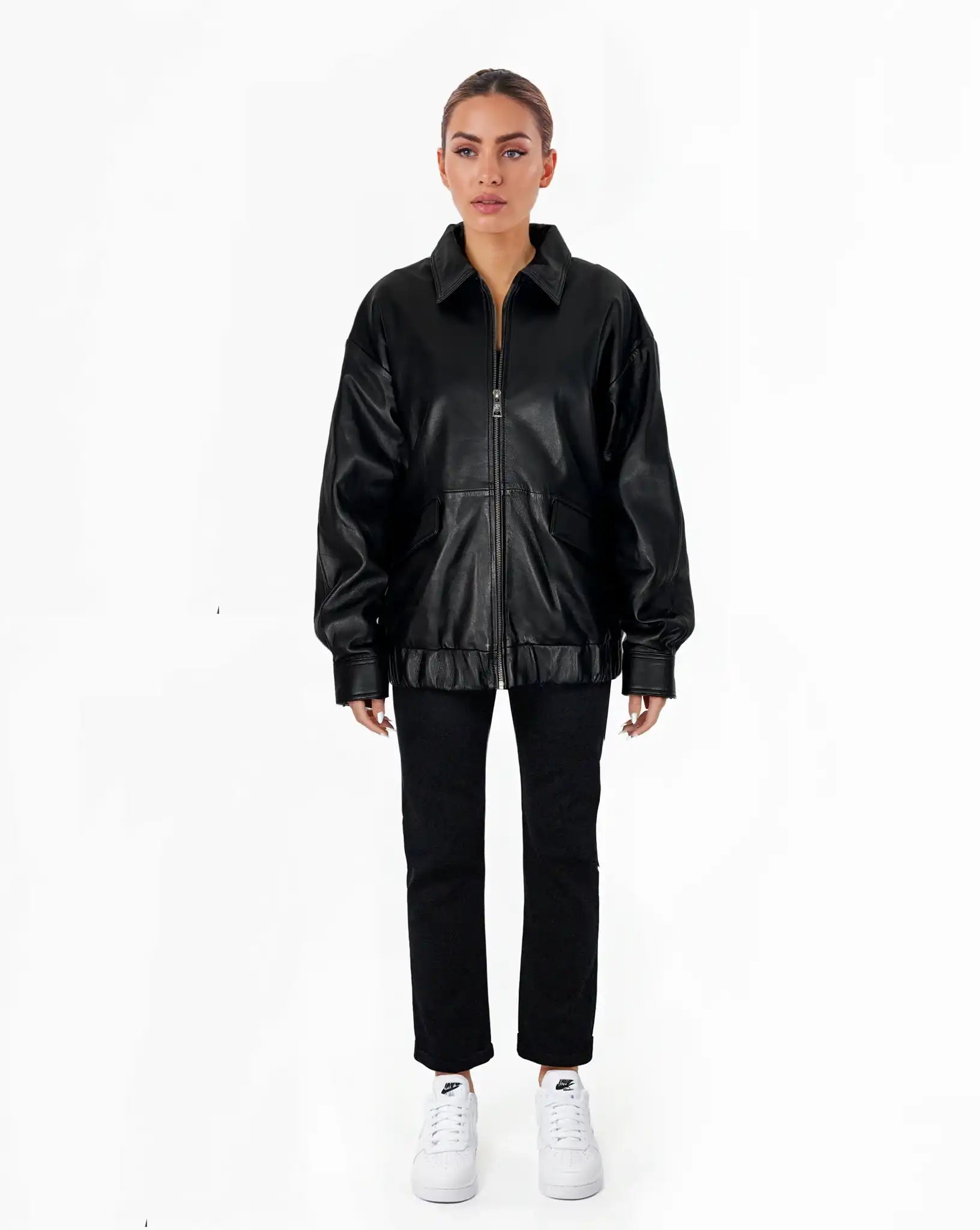 Eine Person steht mit dem Gesicht nach vorne vor einem schlichten weißen Hintergrund und trägt eine trueprodigy Nova Oversize-Lederjacke mit Gummizugsaum & Lederdetails, eine schwarze Hose und weiße Turnschuhe, wobei die Arme entspannt an der Seite liegen.