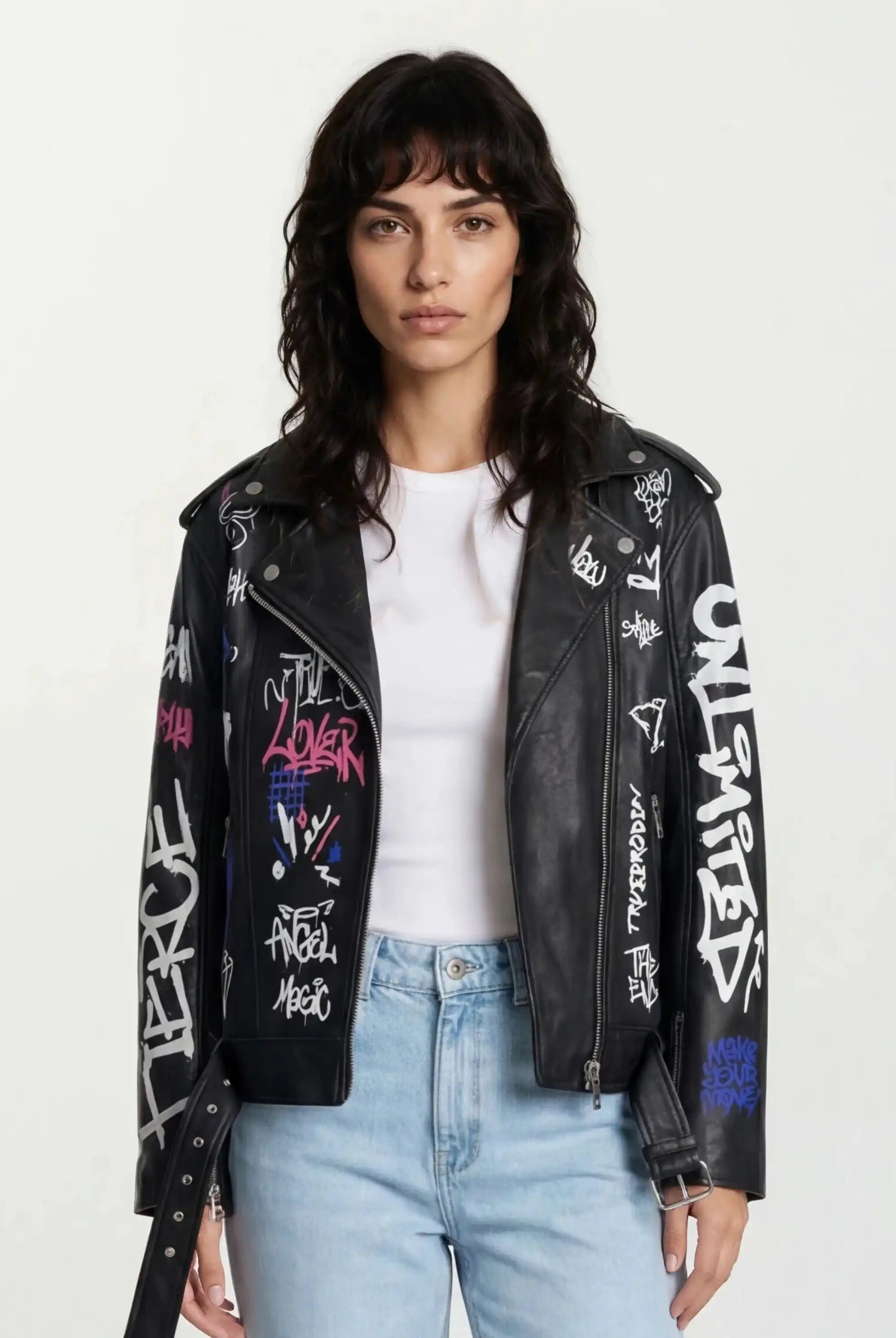Eine Frau mit gewelltem dunklem Haar trägt ein weißes T-Shirt, hellblaue Jeans und eine trueprodigy Feminine Lederjacke mit Grafittiprint und schrägem Reißverschluss vor einem schlichten Hintergrund.
