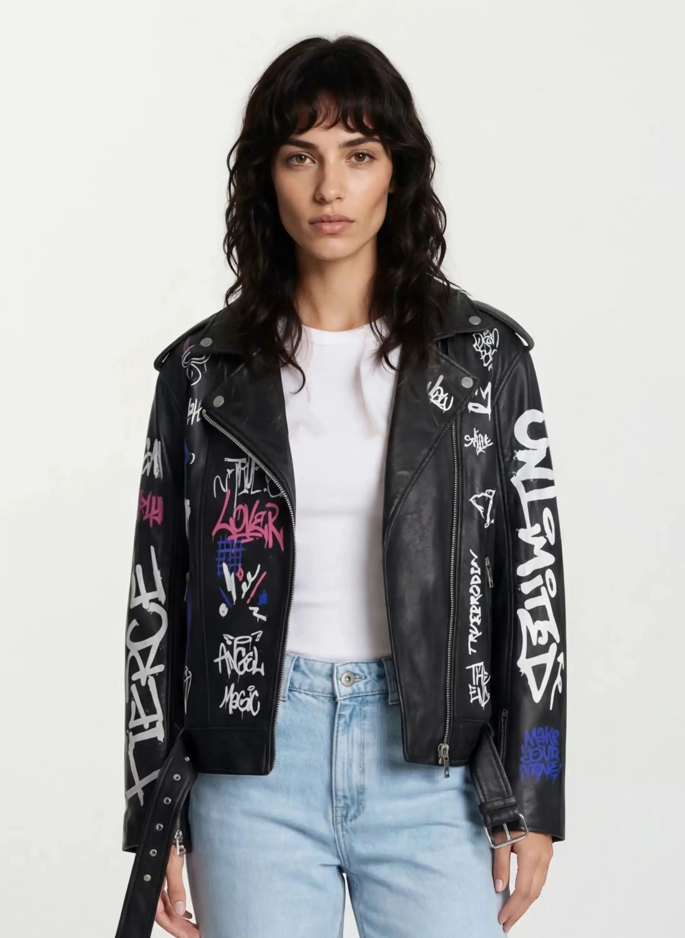 Eine Frau mit gewelltem dunklem Haar trägt ein weißes T-Shirt, hellblaue Jeans und eine trueprodigy Feminine Lederjacke mit Grafittiprint und schrägem Reißverschluss vor einem schlichten Hintergrund.
