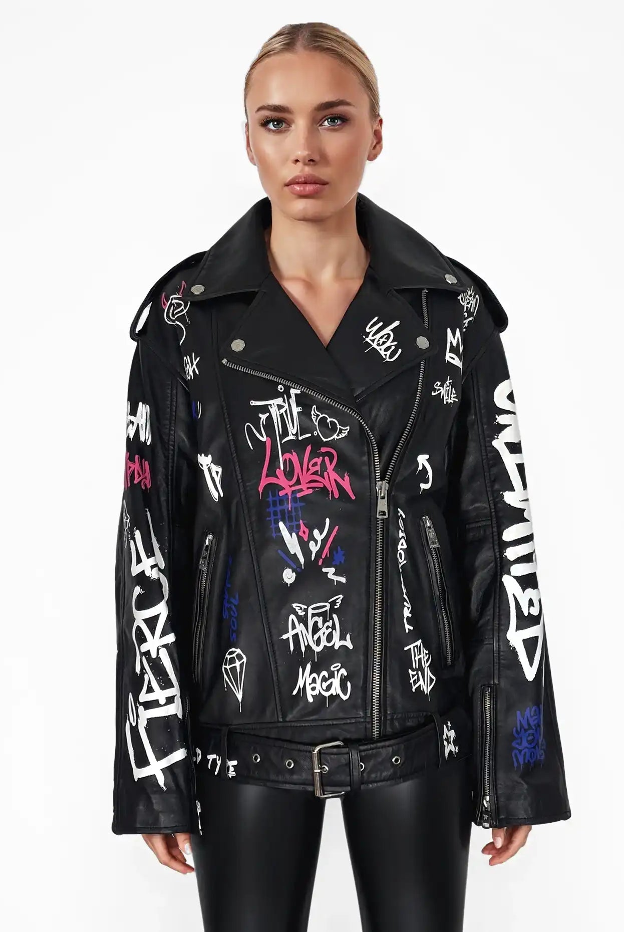 Eine Person blickt nach vorne und trägt die trueprodigy Anya-Lederjacke mit weißen und bunten Graffiti-Schriftzügen und Zeichnungen, gepaart mit einer schwarzen, glänzenden Hose vor einem schlichten weißen Hintergrund.