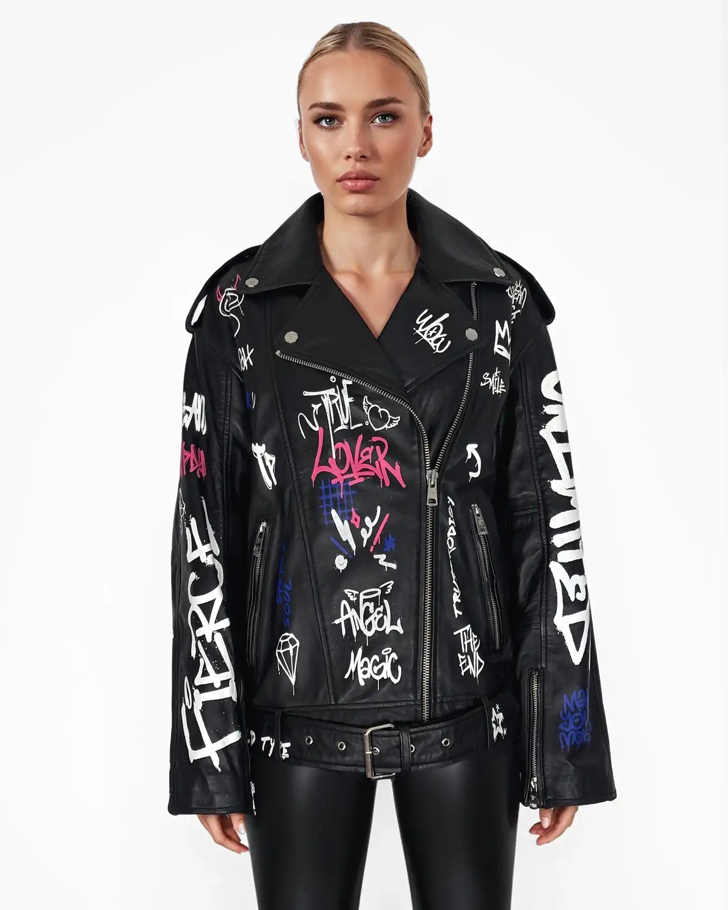 Eine Person blickt nach vorne und trägt die trueprodigy Anya-Lederjacke mit weißen und bunten Graffiti-Schriftzügen und Zeichnungen, gepaart mit einer schwarzen, glänzenden Hose vor einem schlichten weißen Hintergrund.